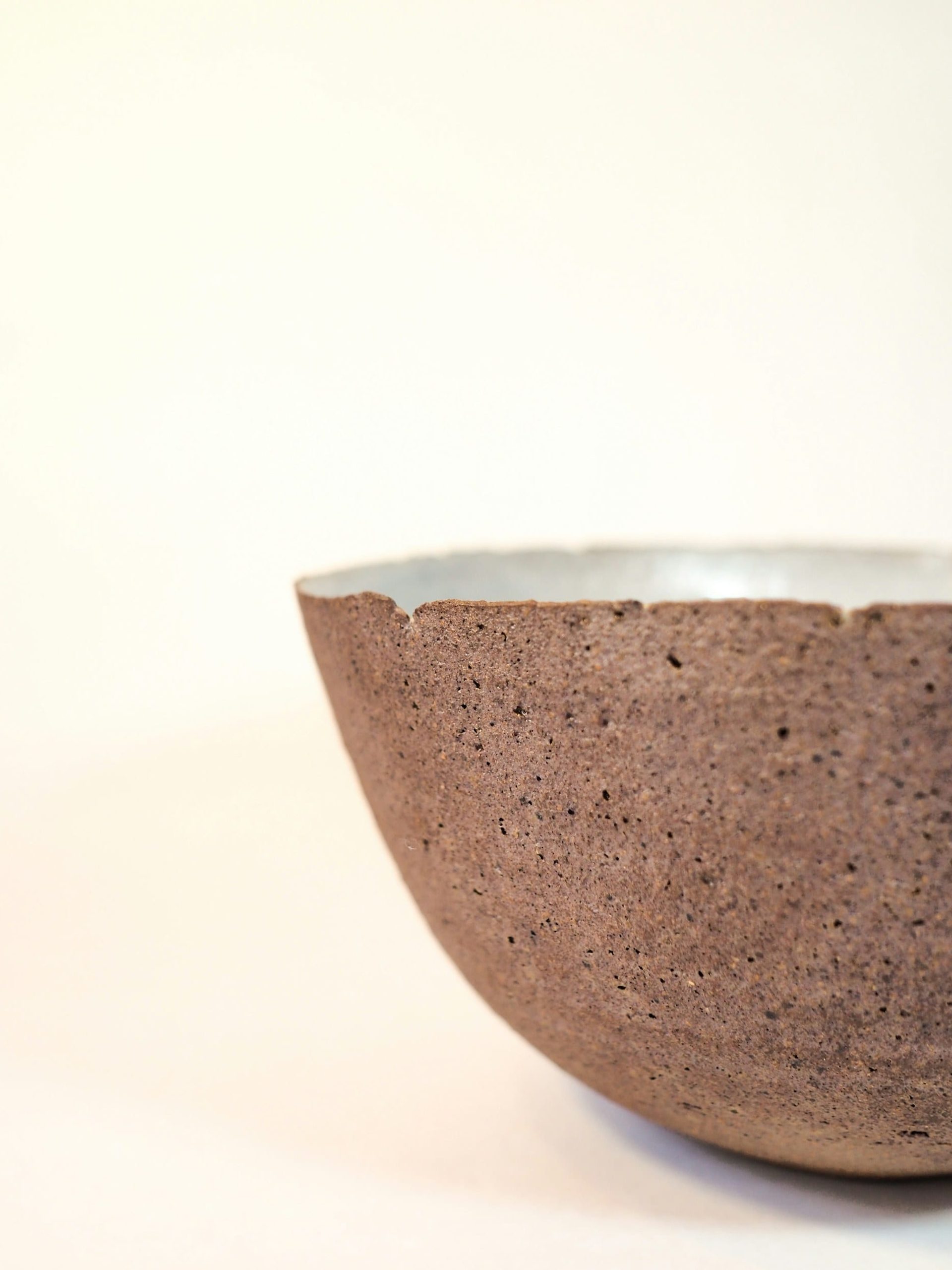 A coarse unglazed clay bowl with a smooth white glazed interior, lit against a pale ground