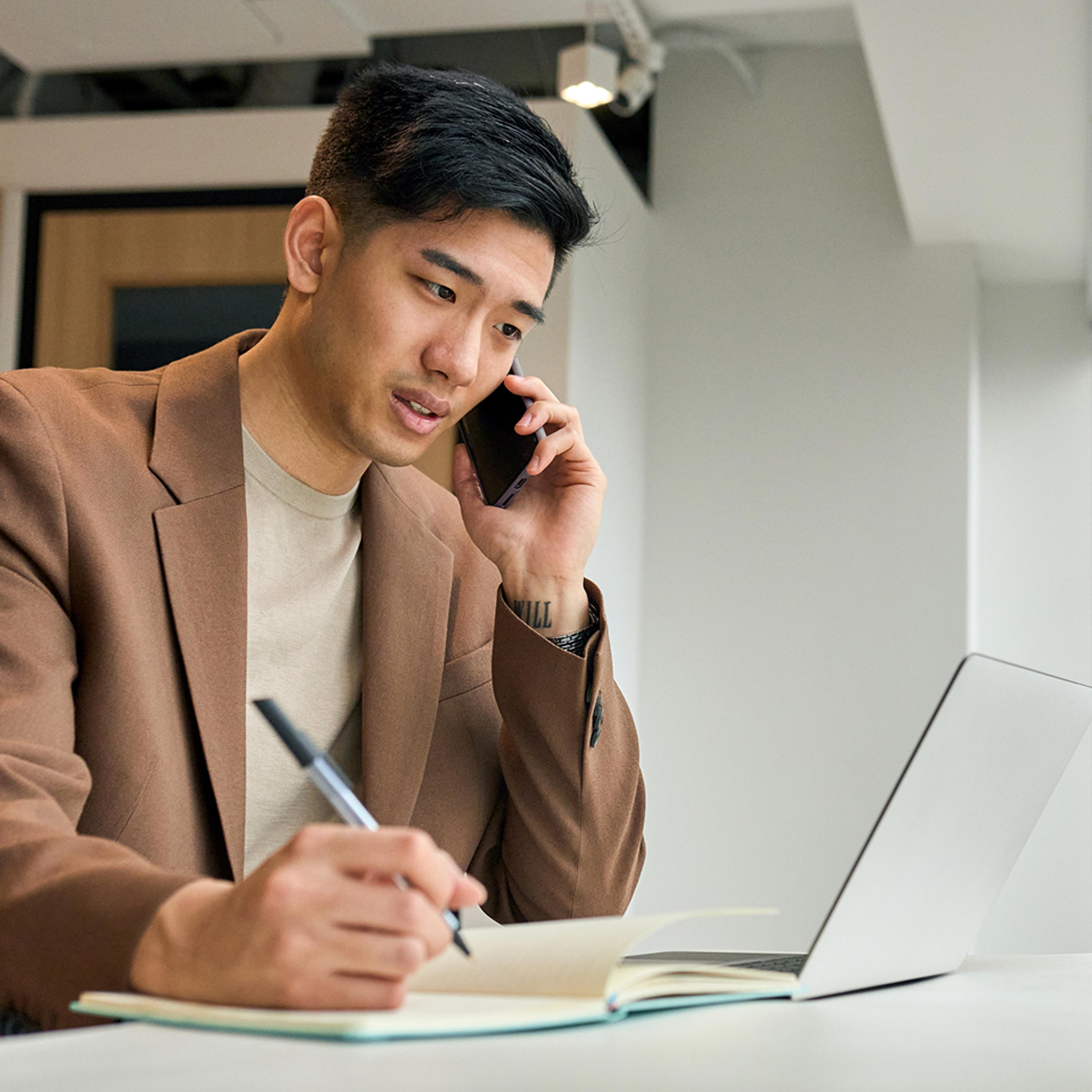 man taking notes while on phone
