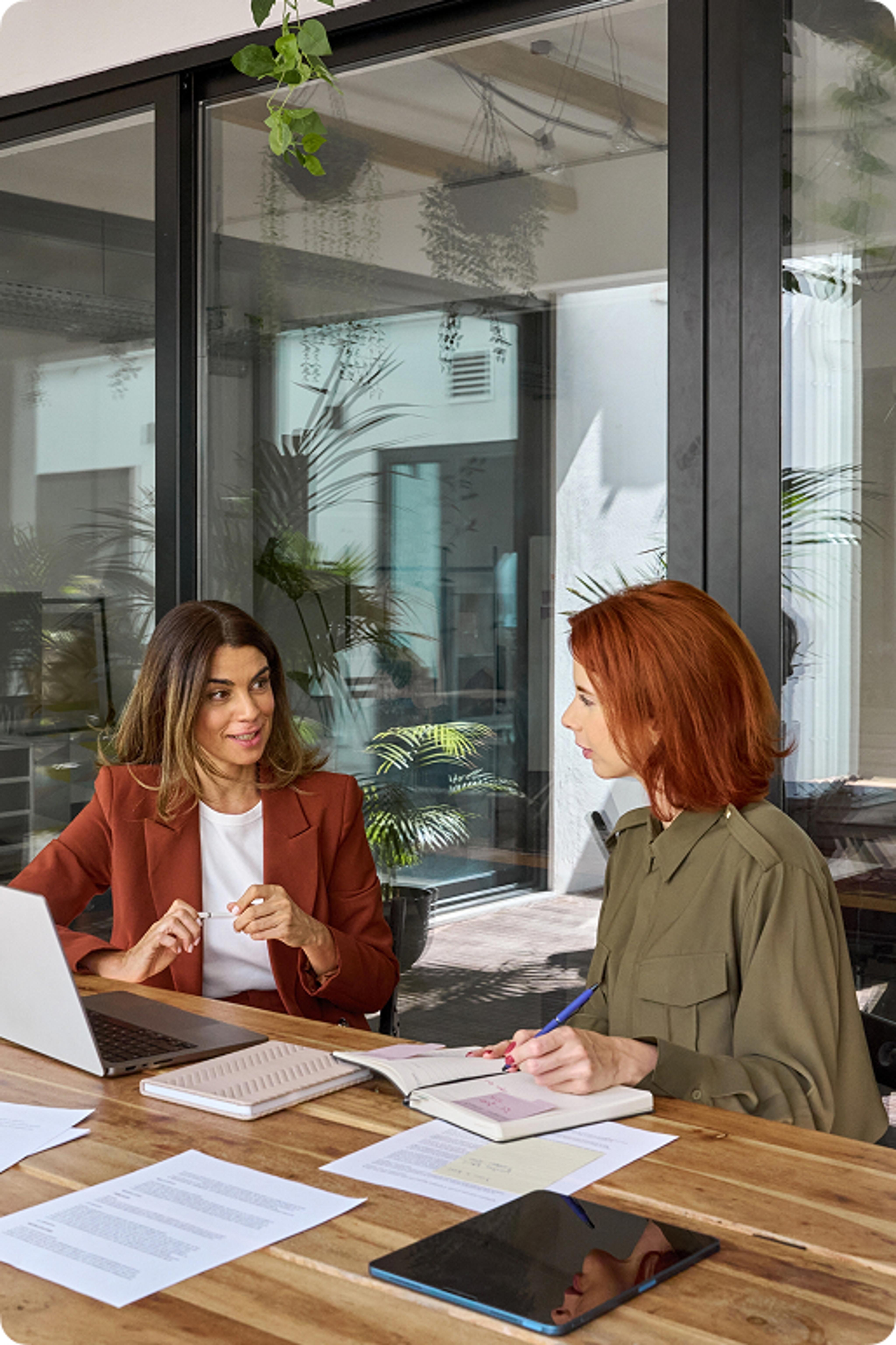 Photo of two women working together with books and a computer at a desk. 