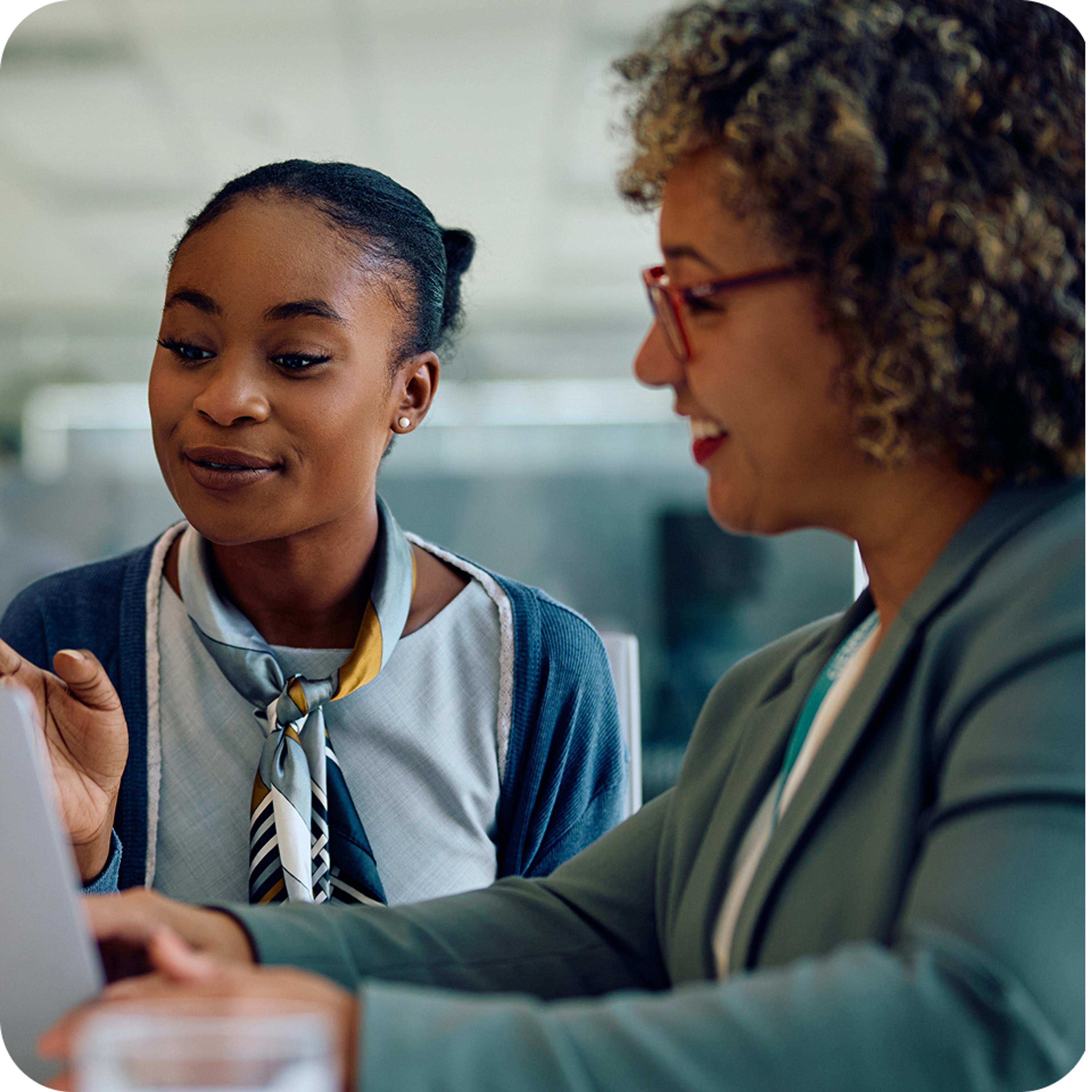 Two women smiling as they work together with a document in front of them.