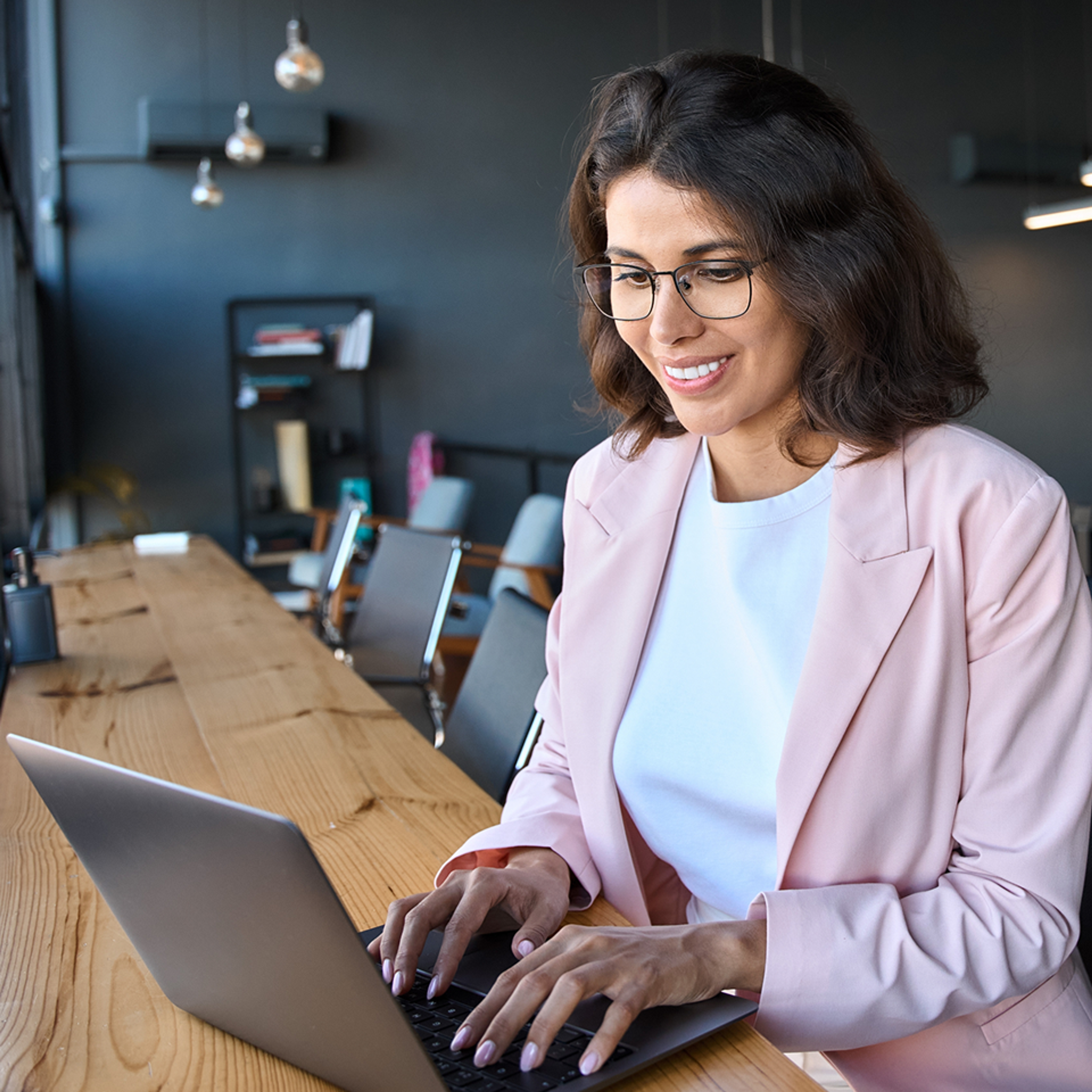 Smiling woman wearing glasses working on a laptop. 