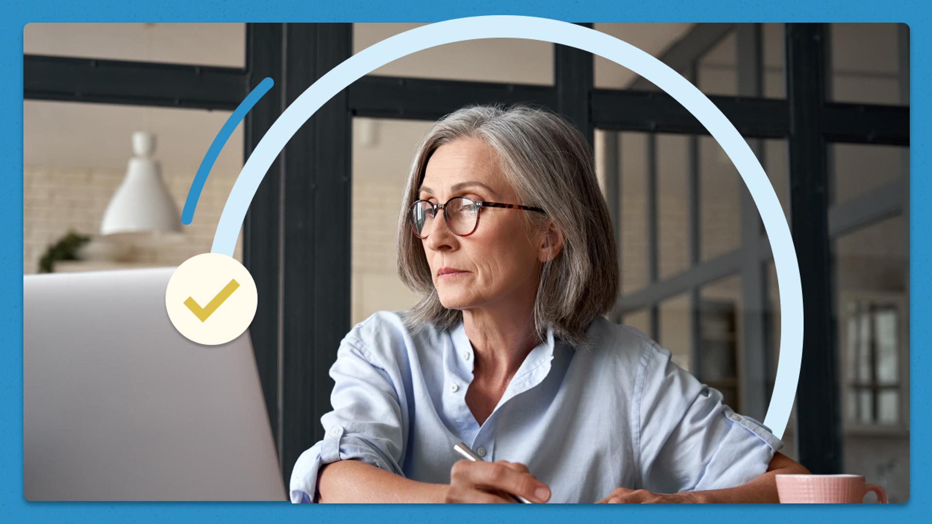 A woman with gray hair and glasses sits at a desk, looking thoughtfully at a laptop while holding a pen. She appears to be working or concentrating. A light blue semi-circle graphic and a yellow checkmark icon overlay the image.