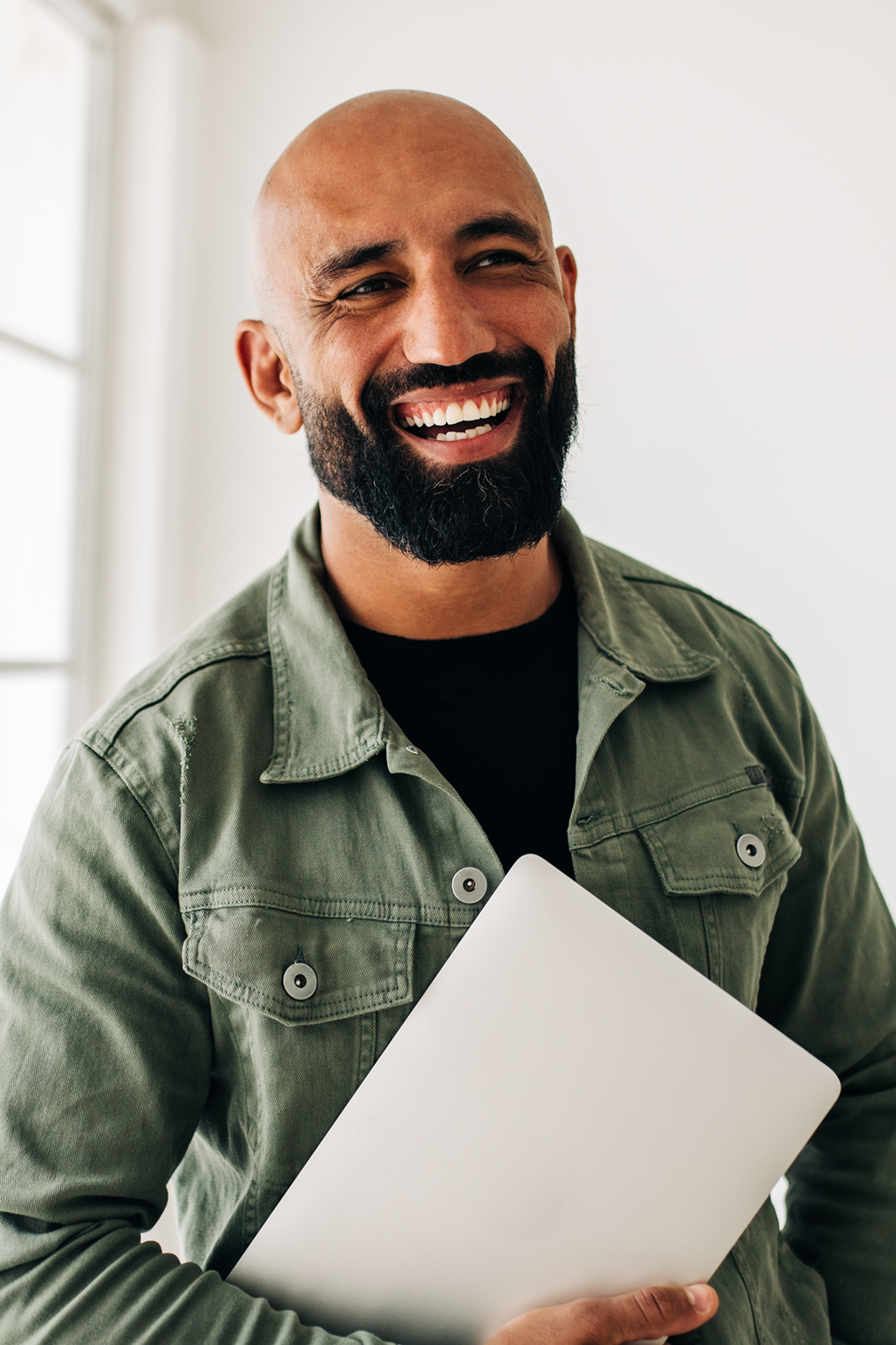 Bearded man smiling while holding a closed computer