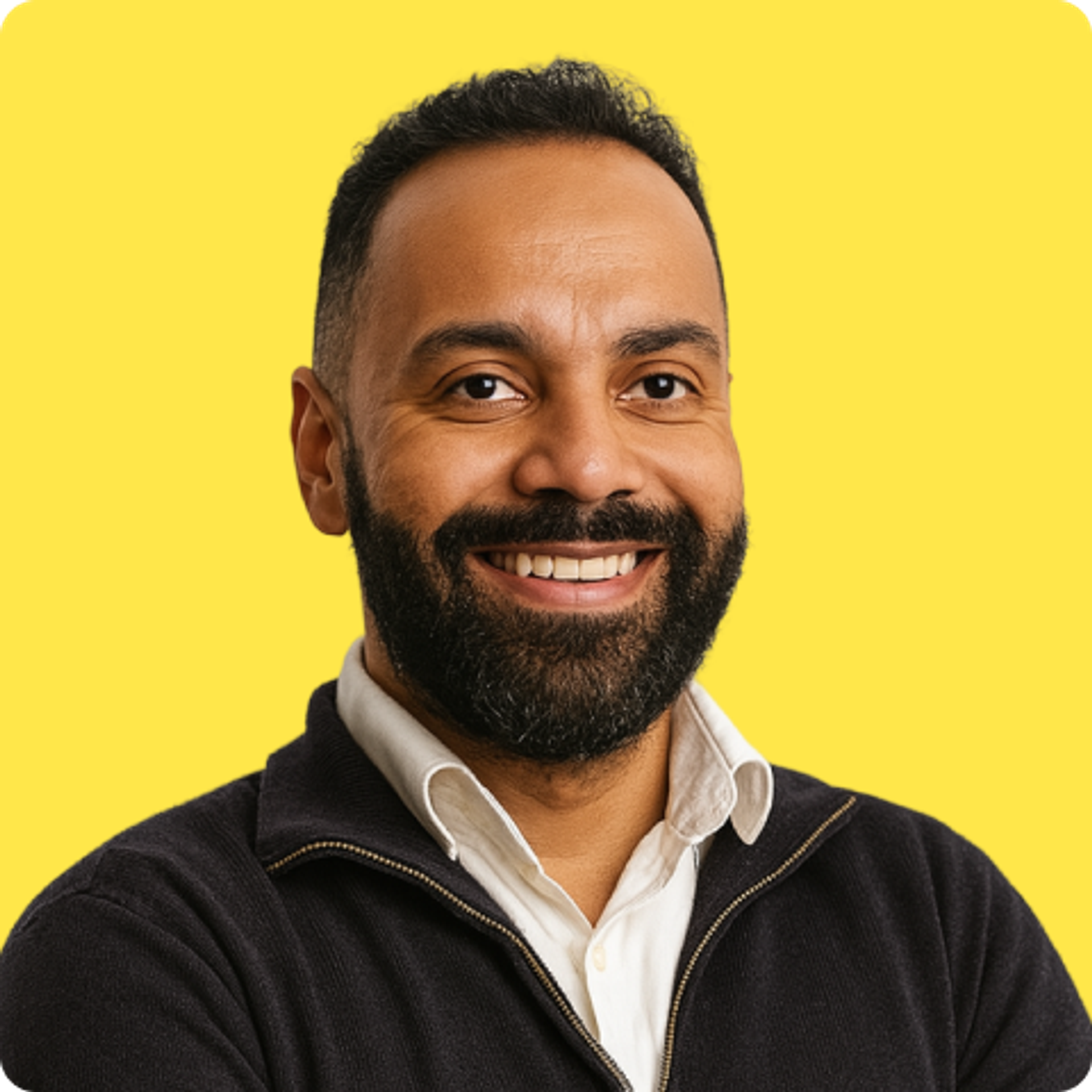 Smiling bearded man with a button up shirt and half-zip in front of a plain yellow background.