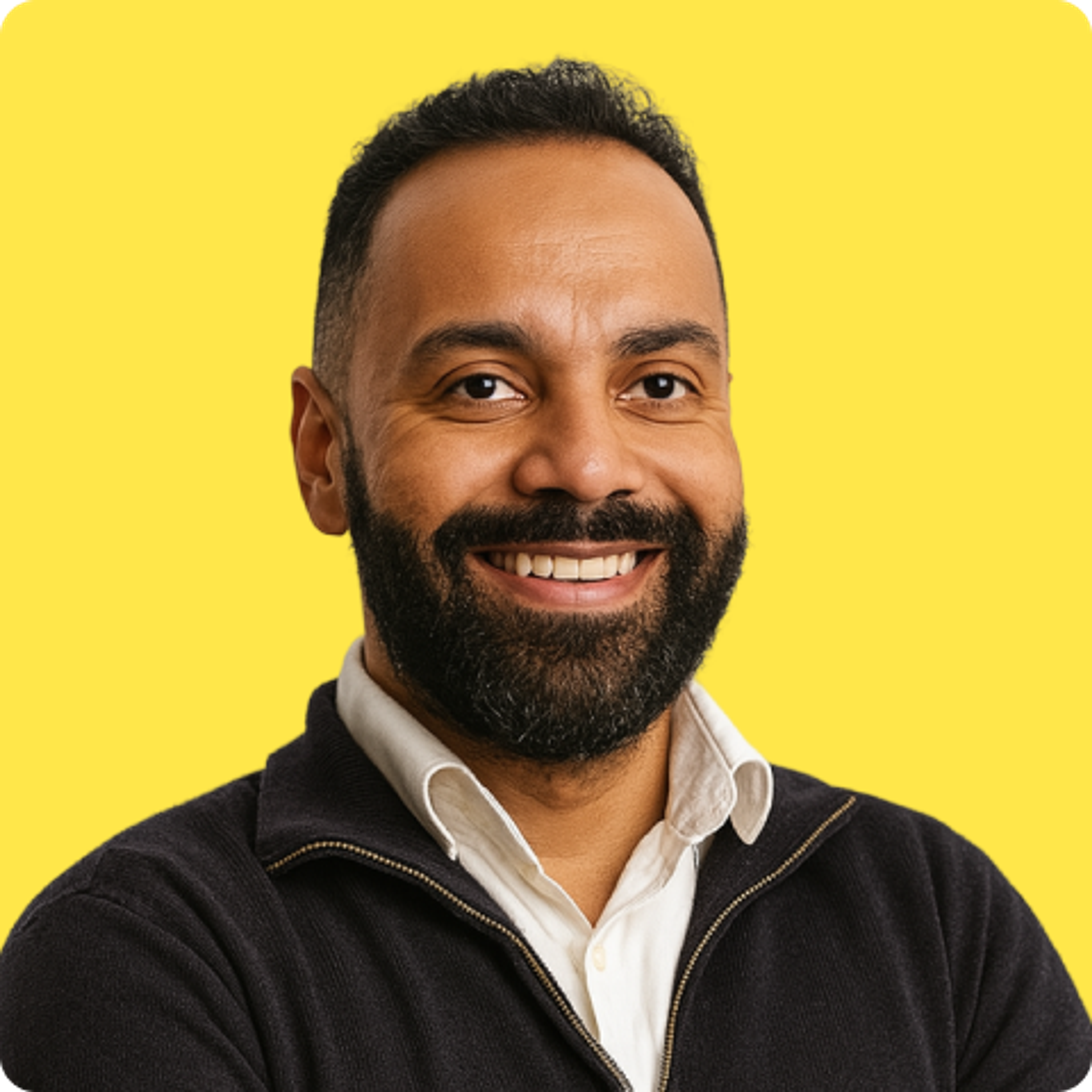 Smiling bearded man with a button up shirt and half-zip in front of a plain yellow background.