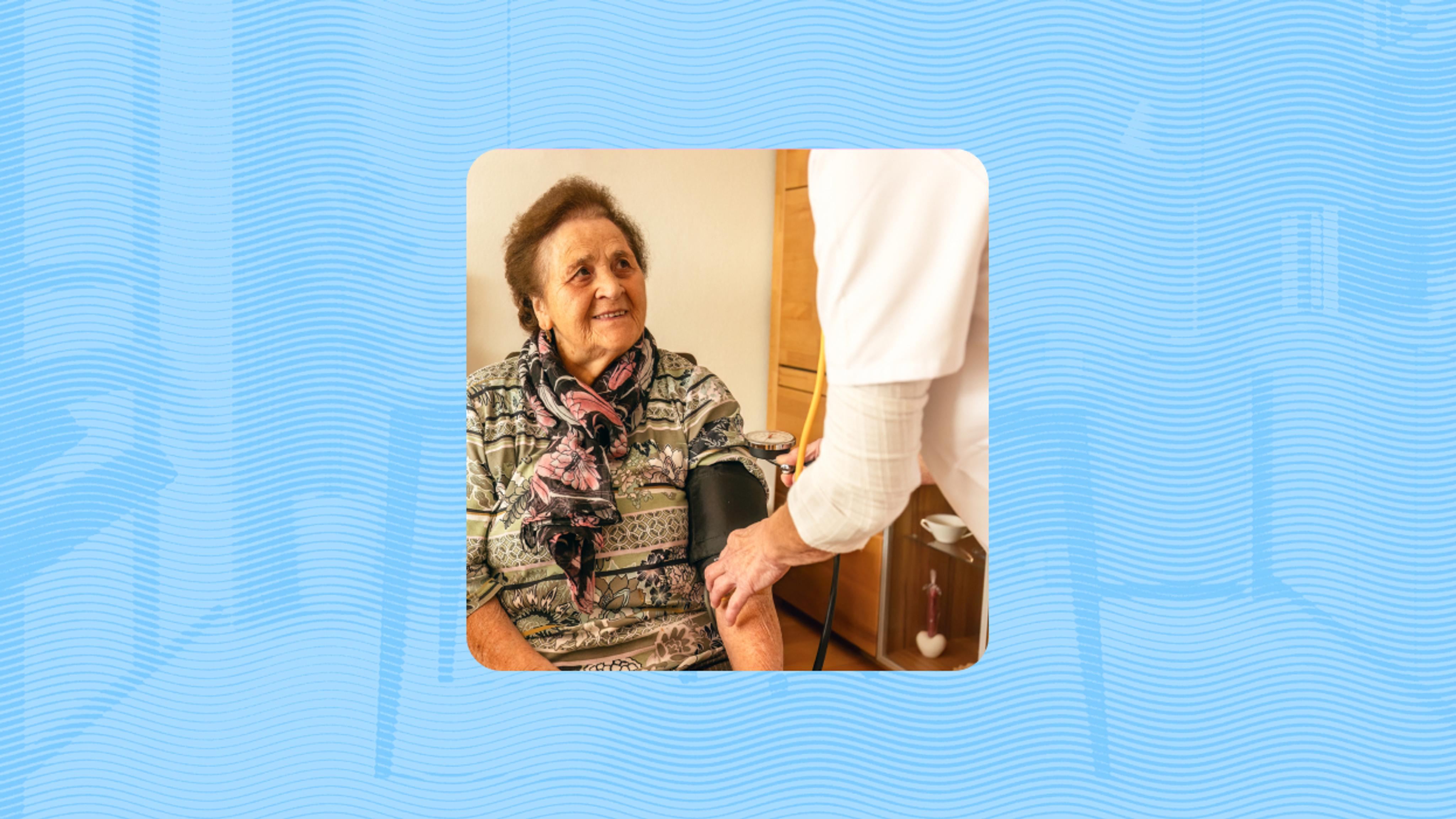 An older woman sits while a healthcare worker measures her blood pressure using an arm cuff.