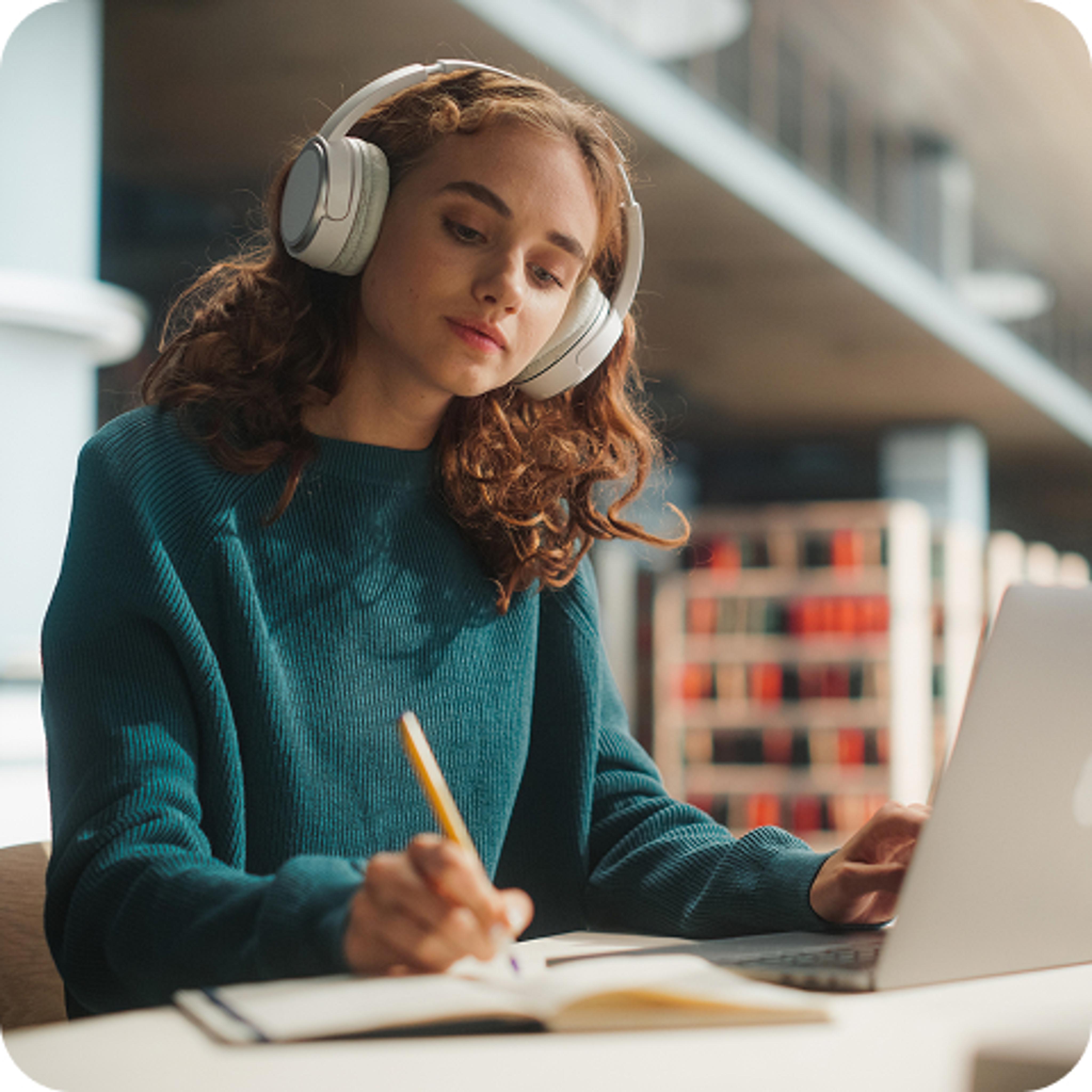 Photo of a young woman studying at a computer while wearing headphones.