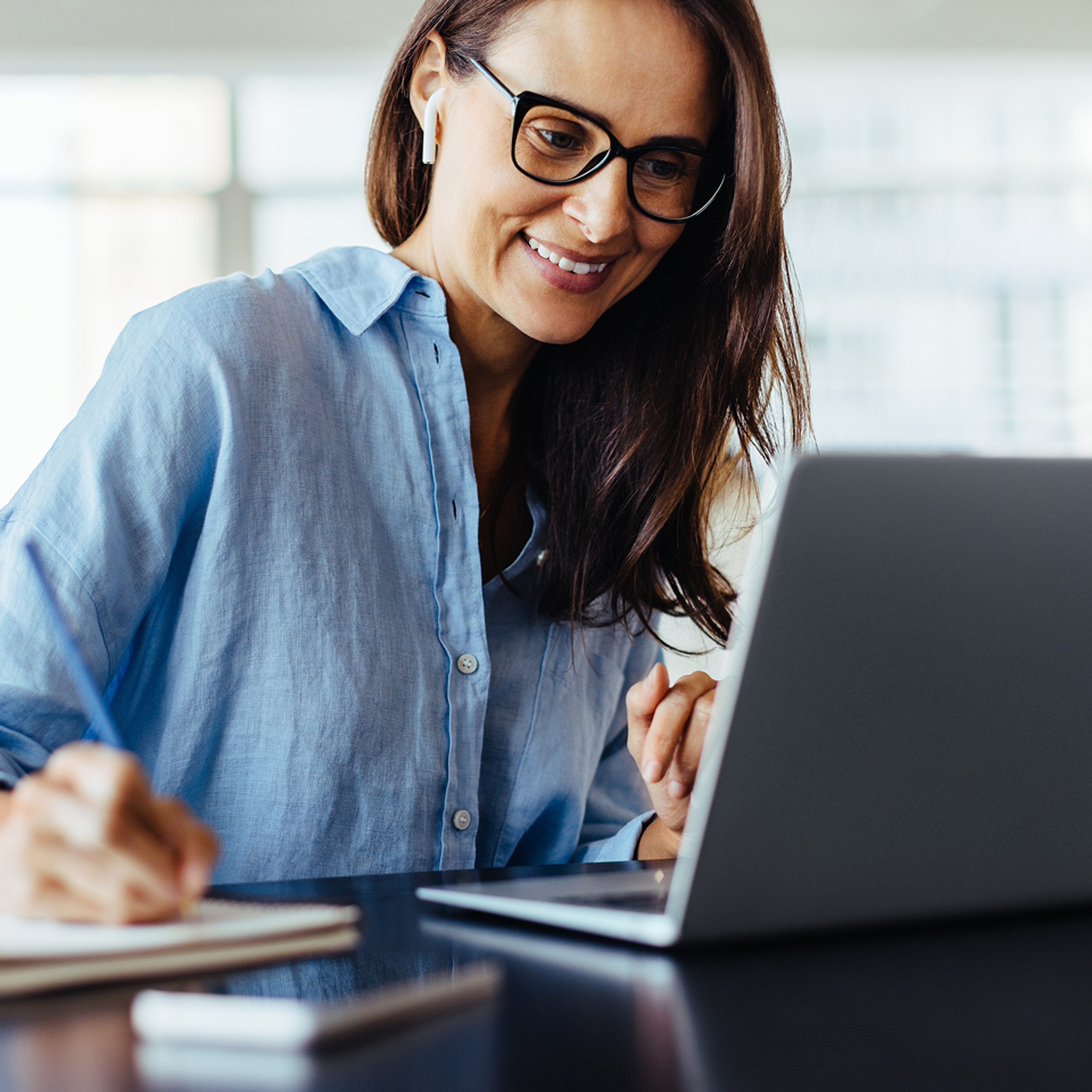 woman taking notes in notebook looking at open laptop