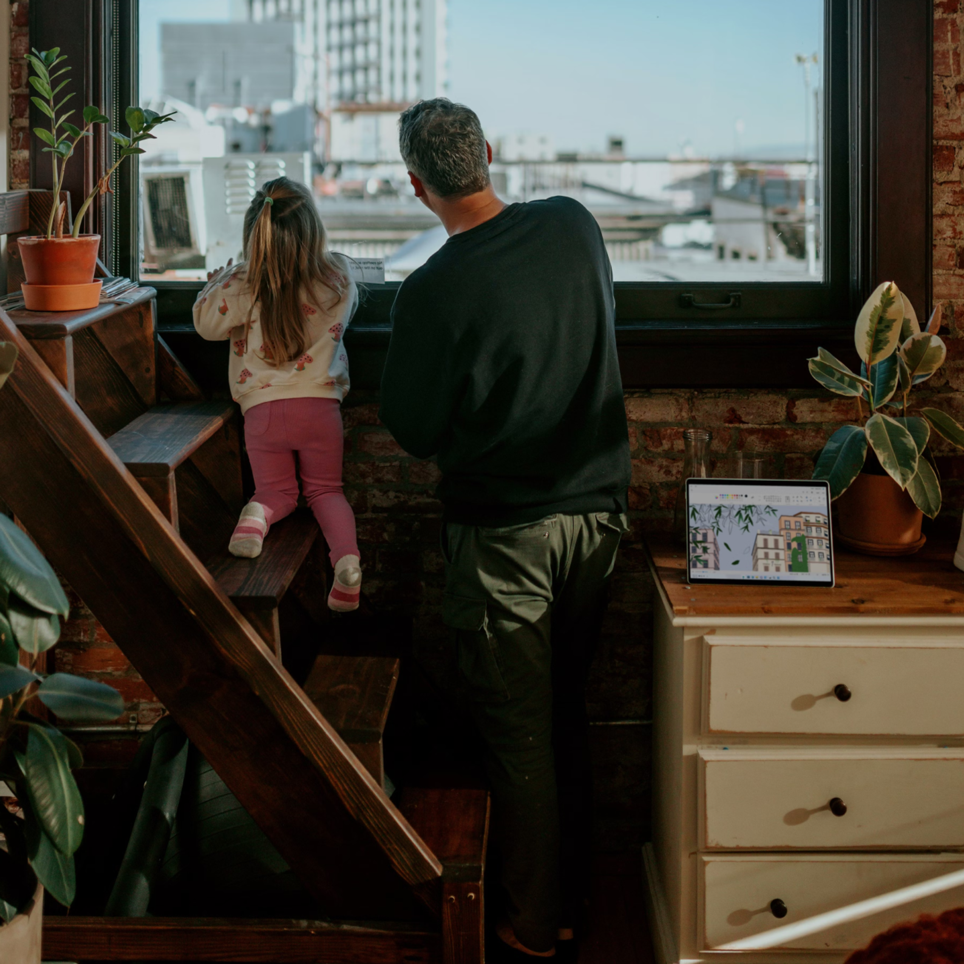 Adult and child looking out a window together in a sunlit home.
