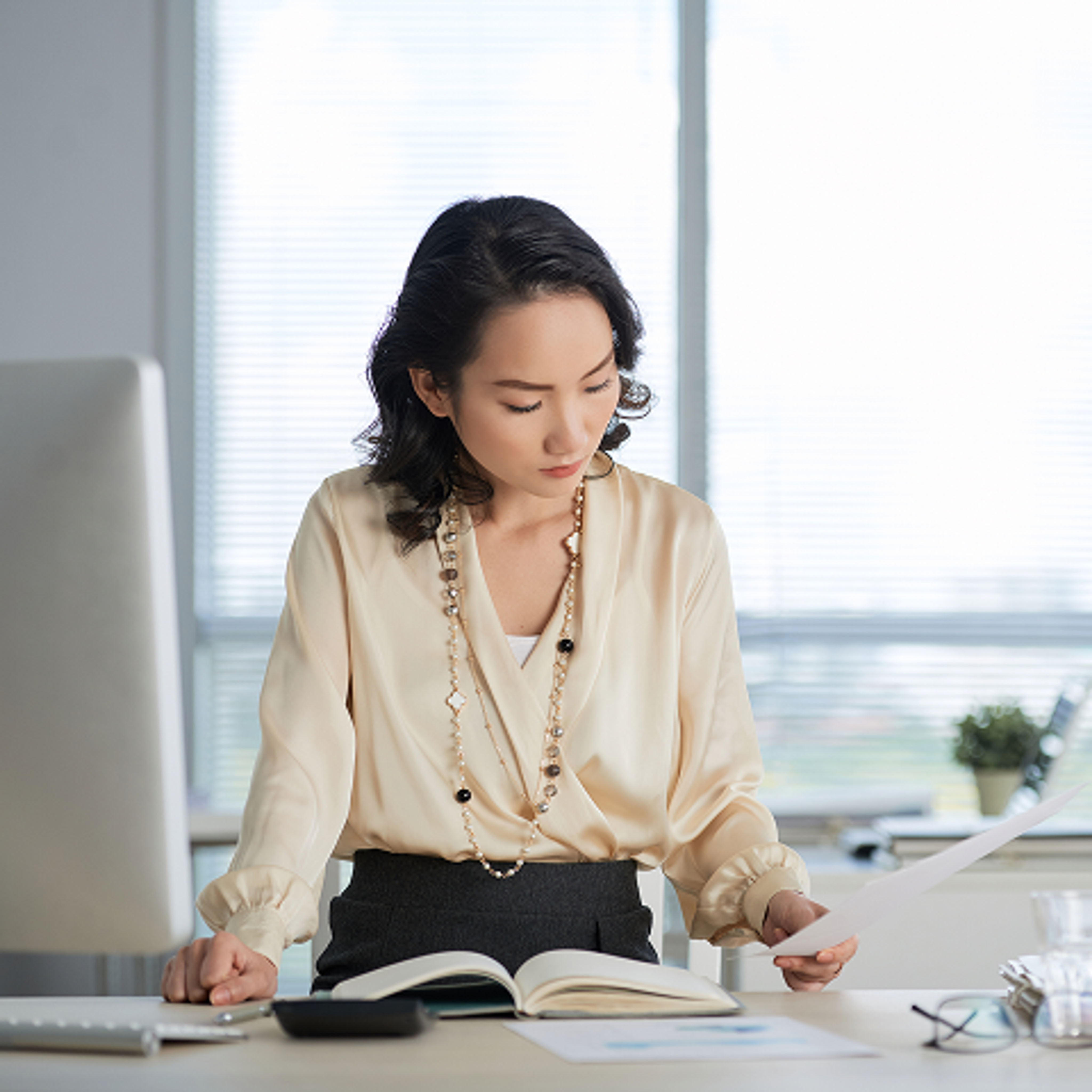 A woman in business attire performs a backbend on outdoor steps, balancing on her forearms and feet, while typing on a laptop placed on the ground in front of her.
