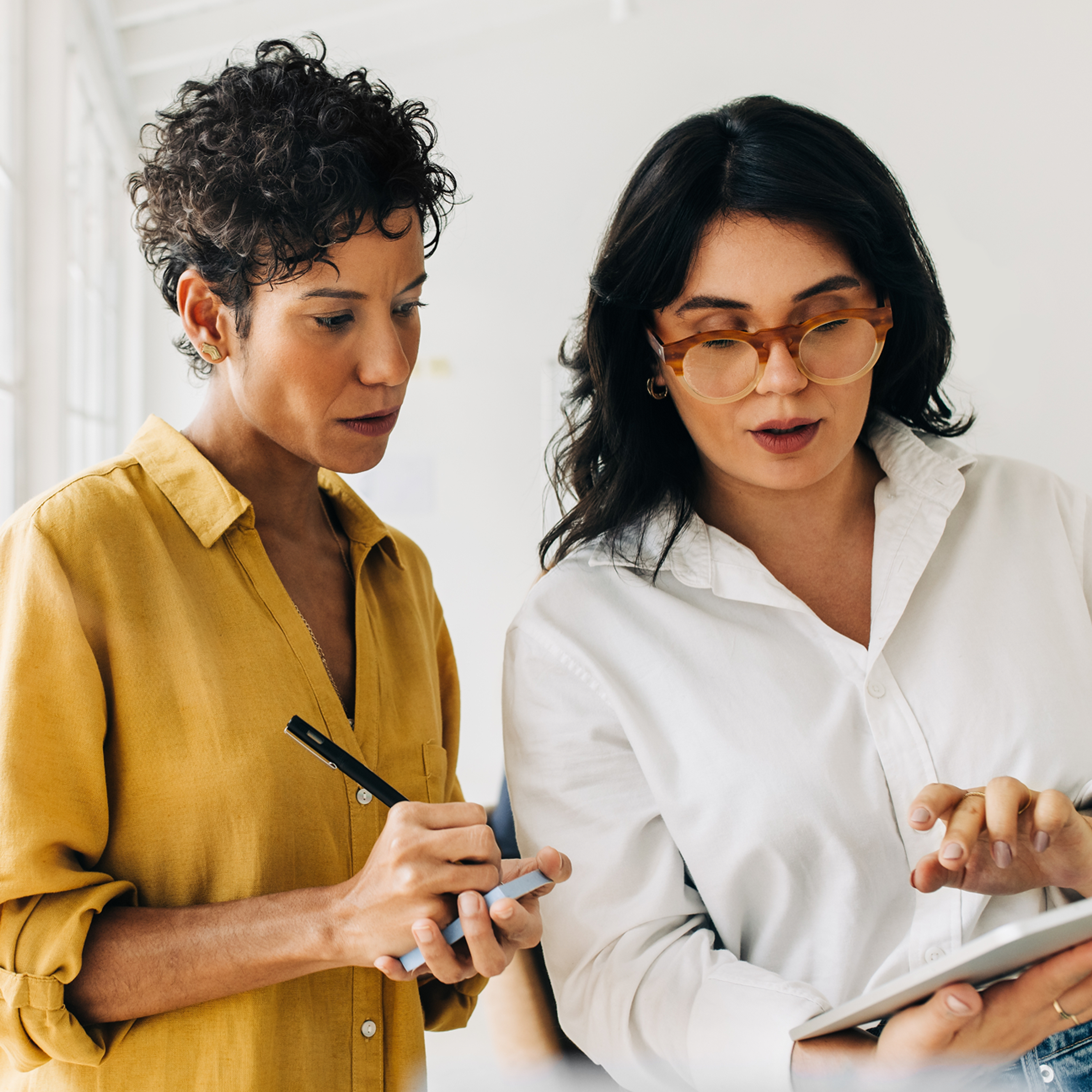 Two women working together with a tablet and a notepad.