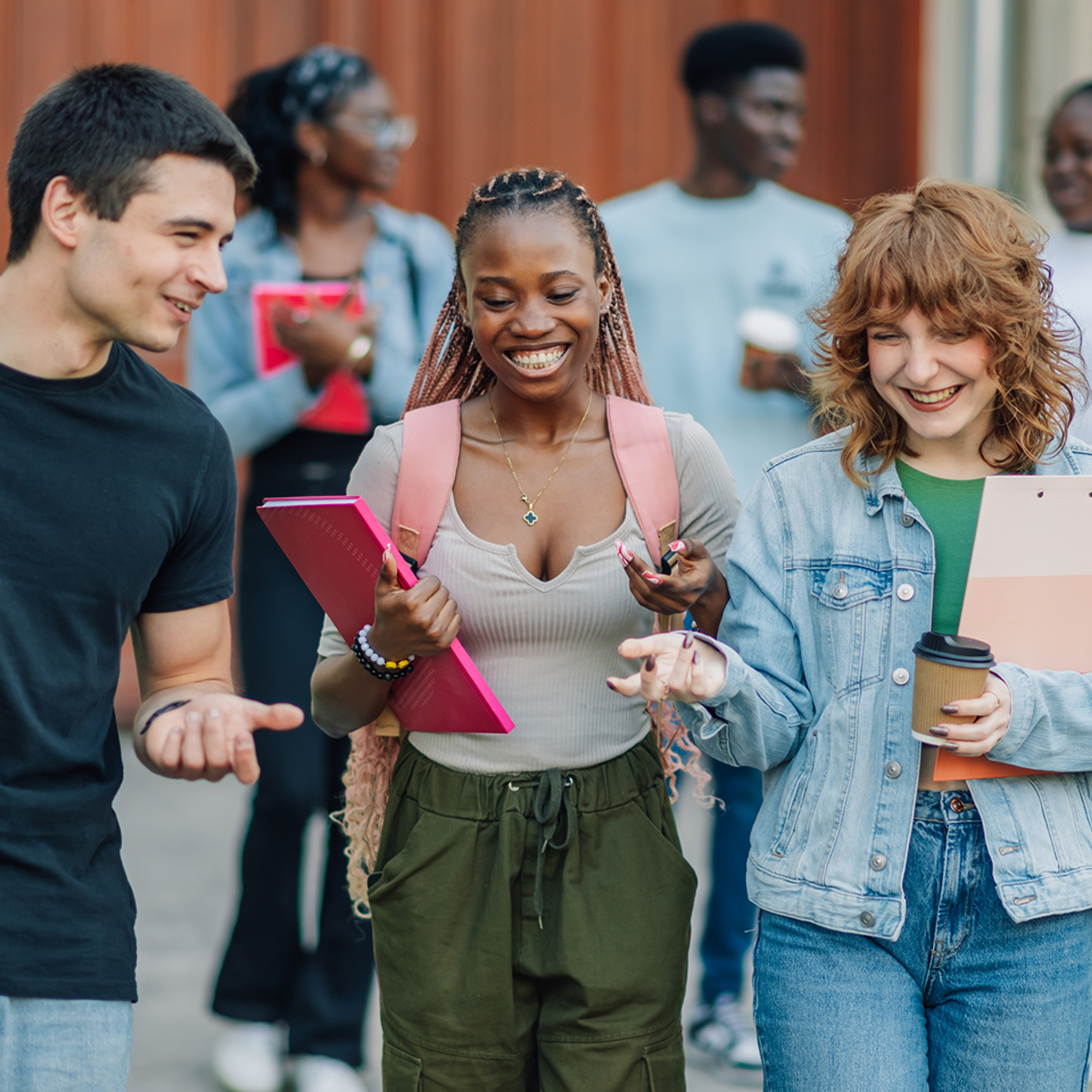A young group of students smiling and talking as they walk and carry their school materials.