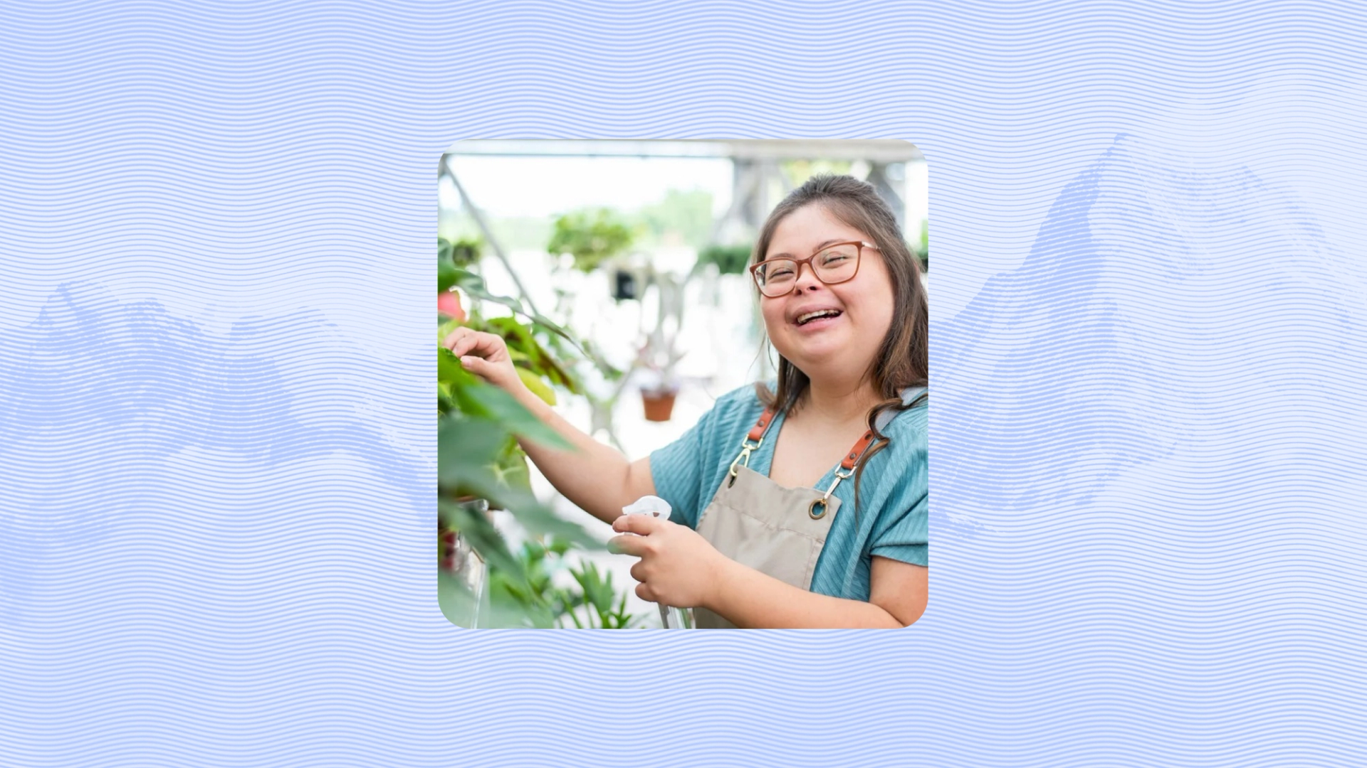 A smiling person wearing glasses and an apron tends to plants inside a bright greenhouse, gently holding leaves while watering.