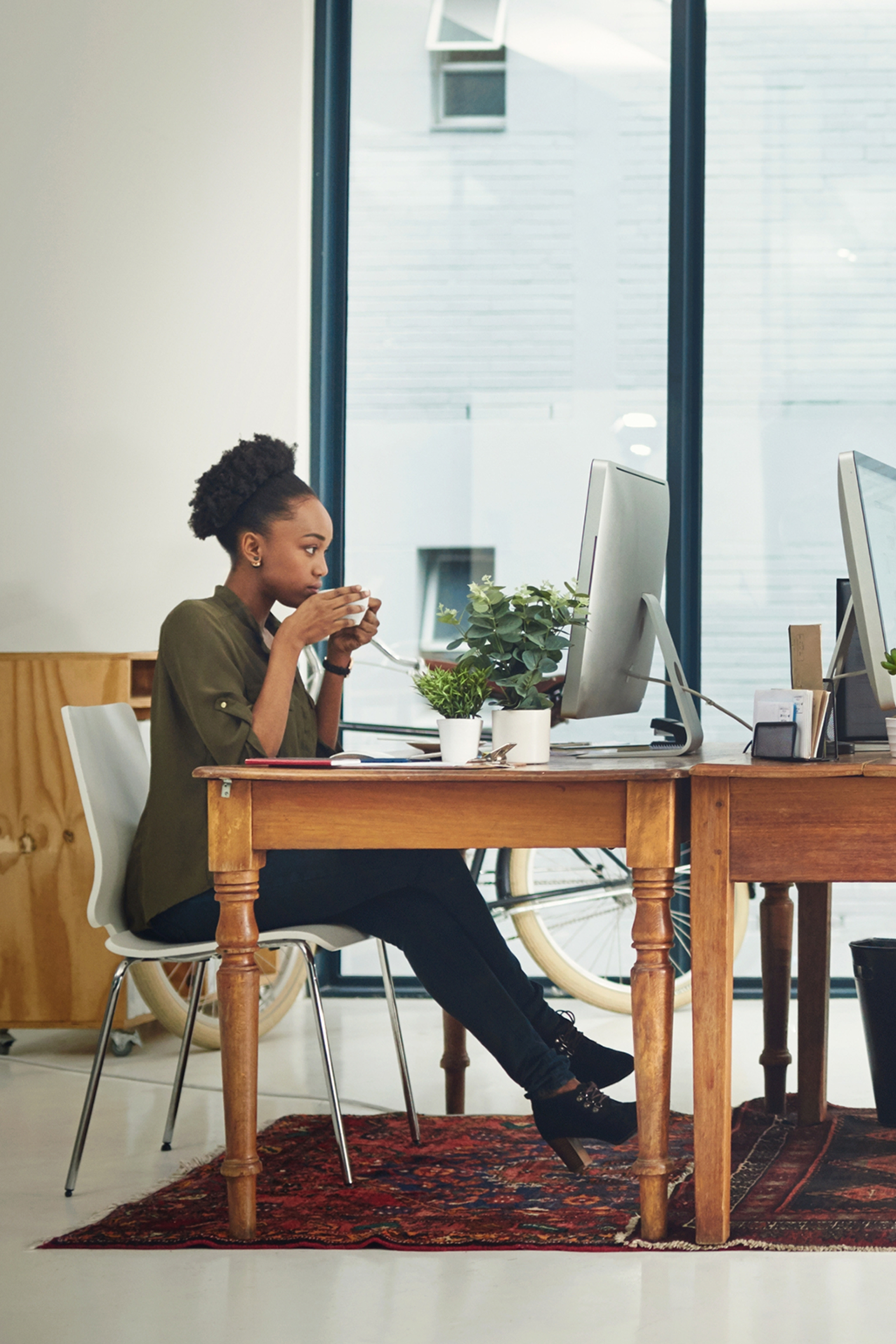 A woman sipping from a coffee cup while working on a computer at a desk.