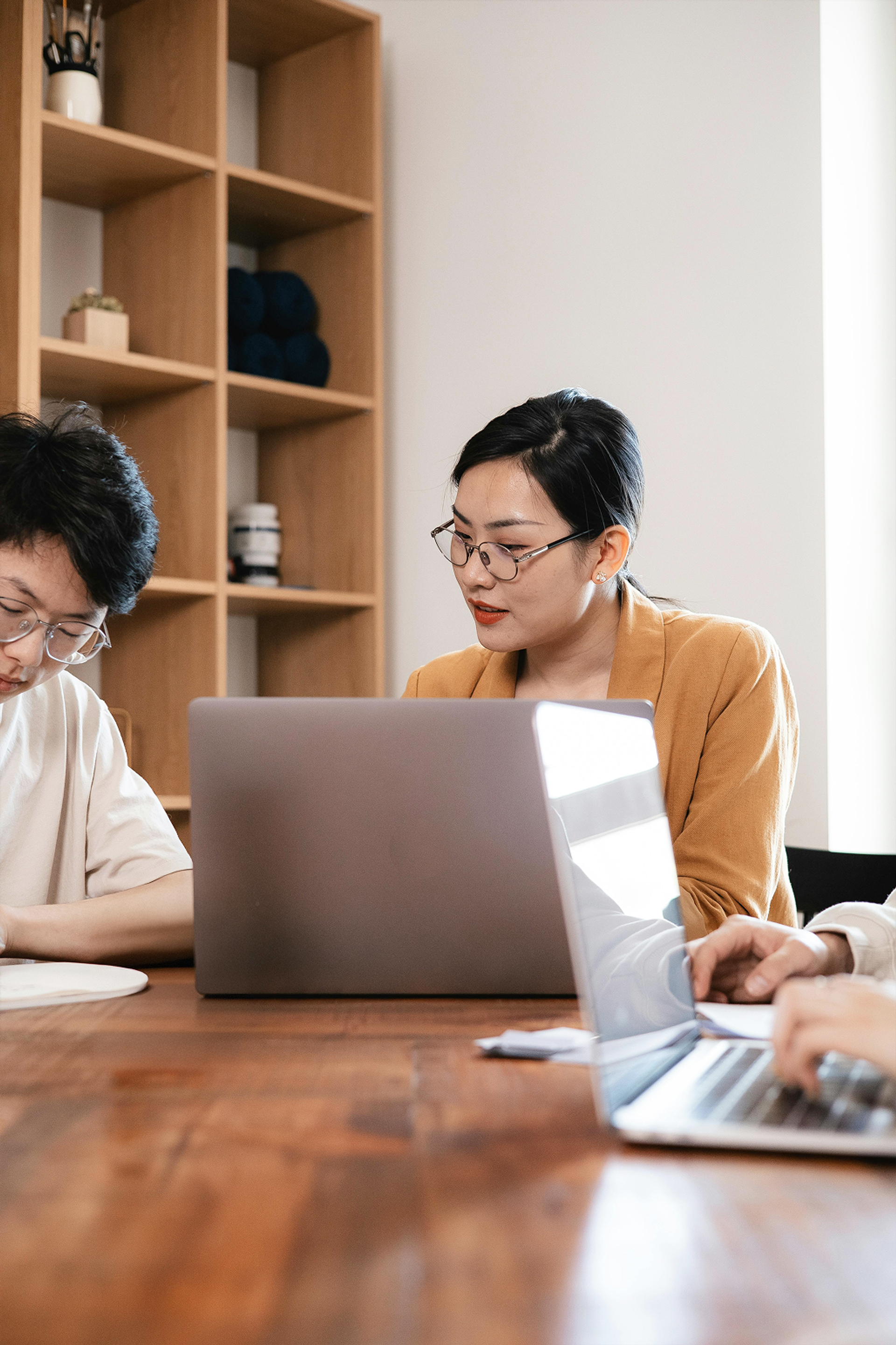 Three colleagues working together at a table with laptops in a bright office. 