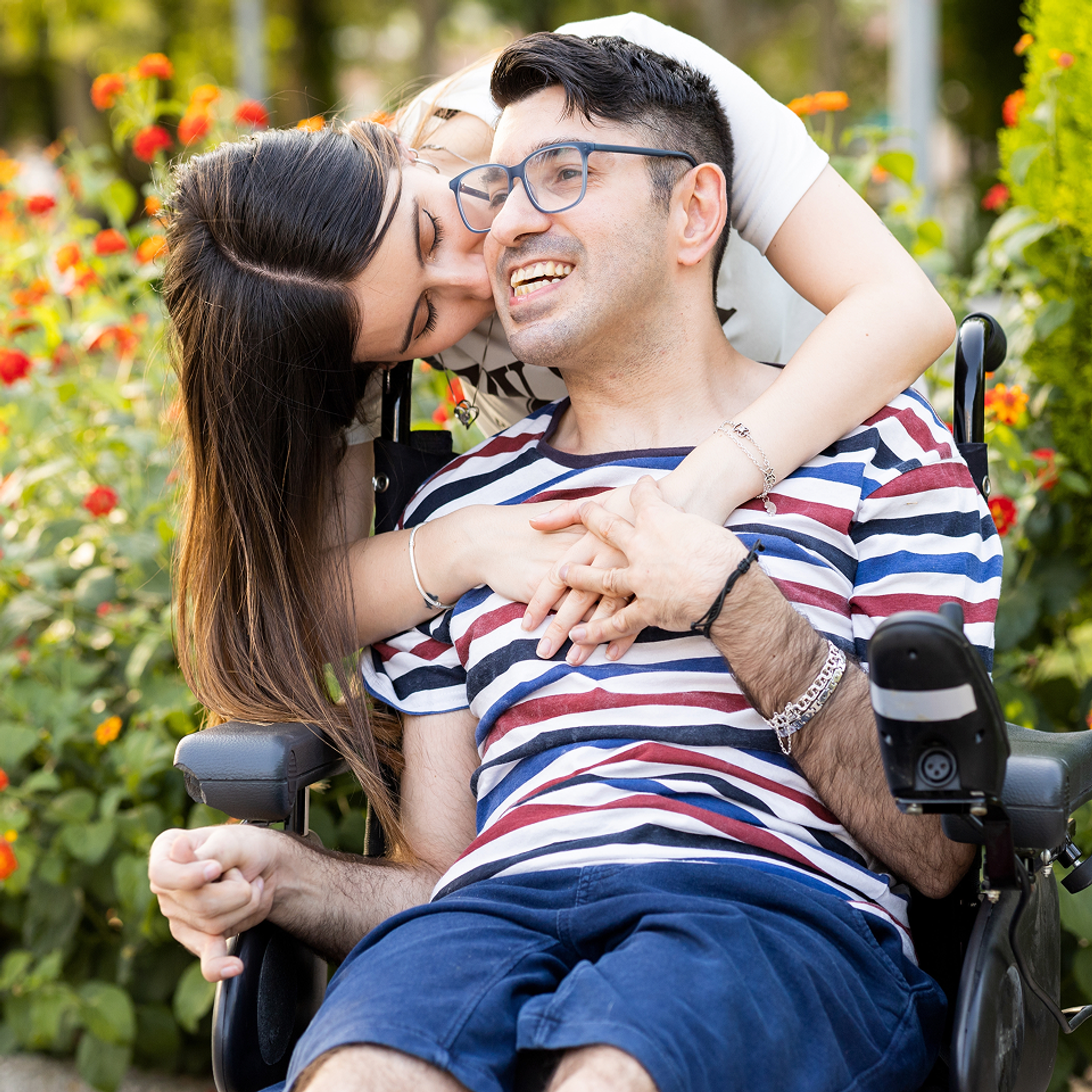 Man in wheelchair receiving a hug from a woman behind him.
