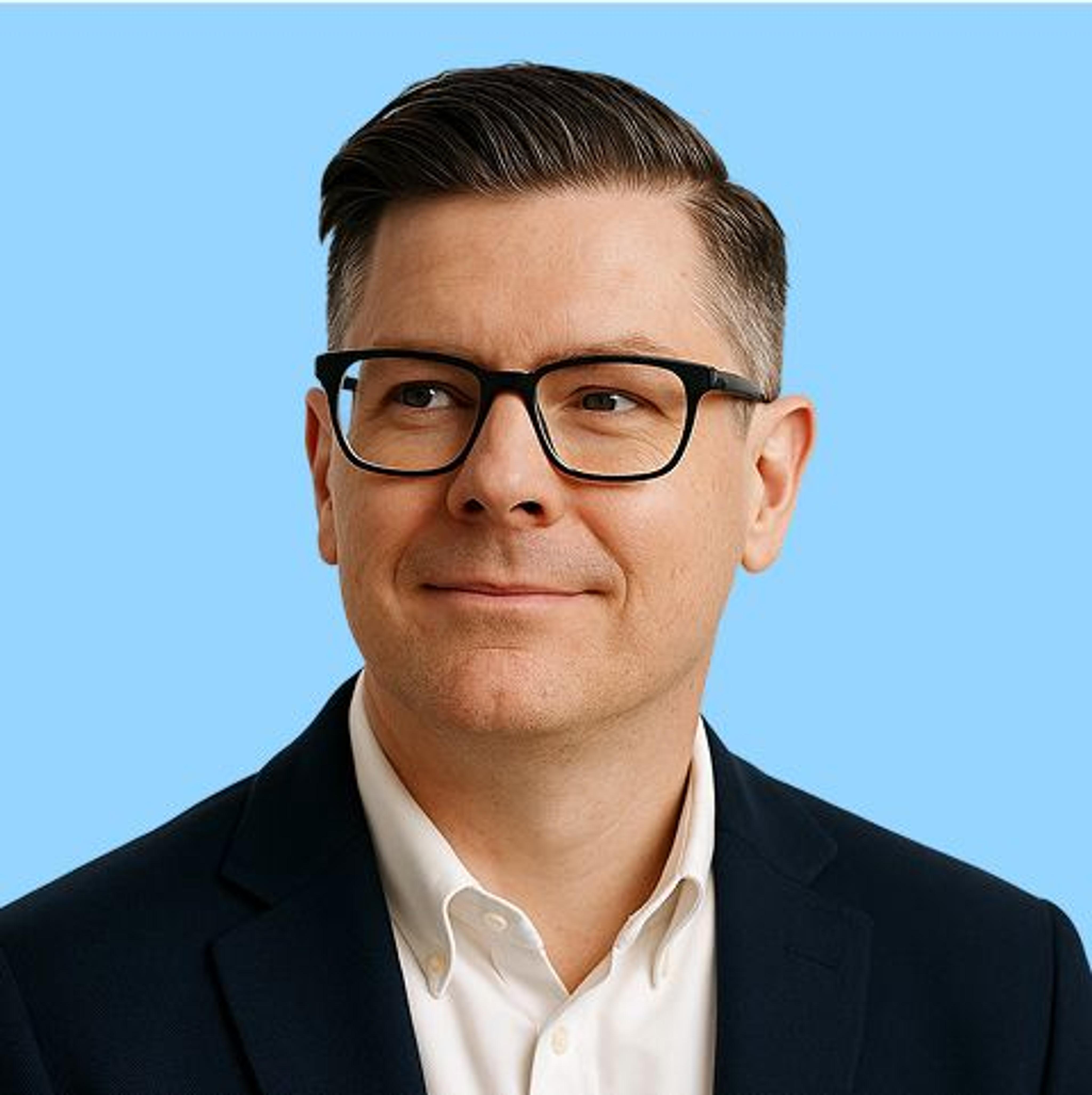 Smiling man in a suit with glasses looking off to the side with a blue background