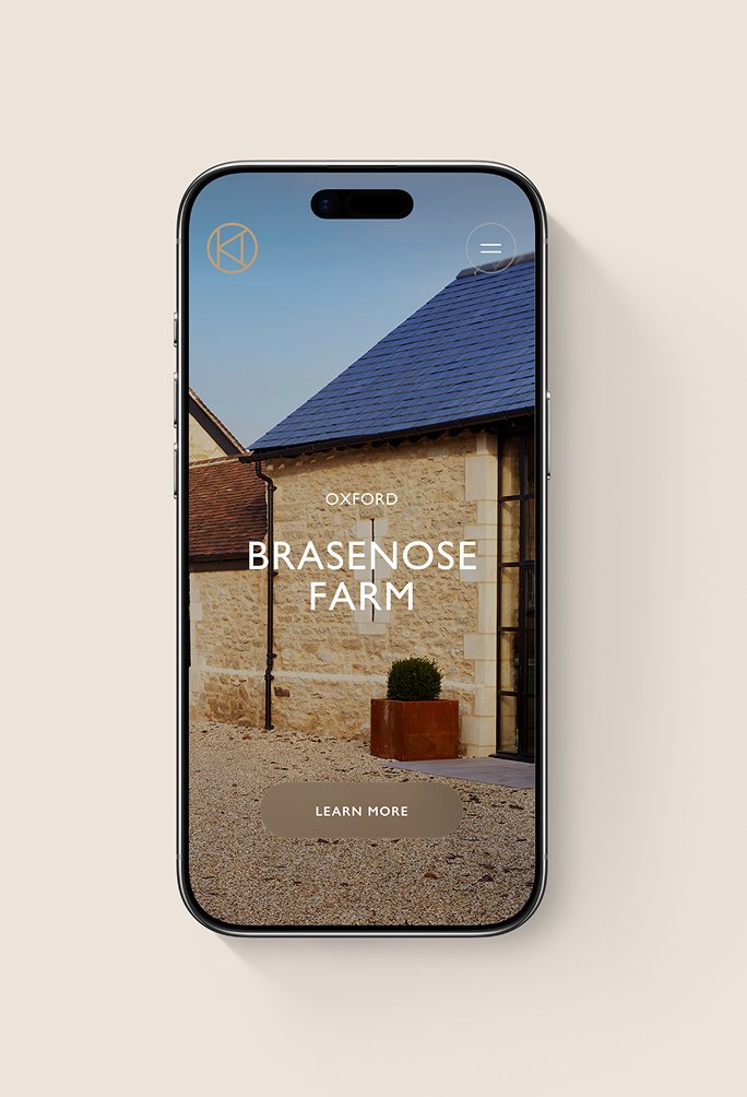 Stone barn with glass entrance beside smartphone showing Brasenose Farm website on beige background