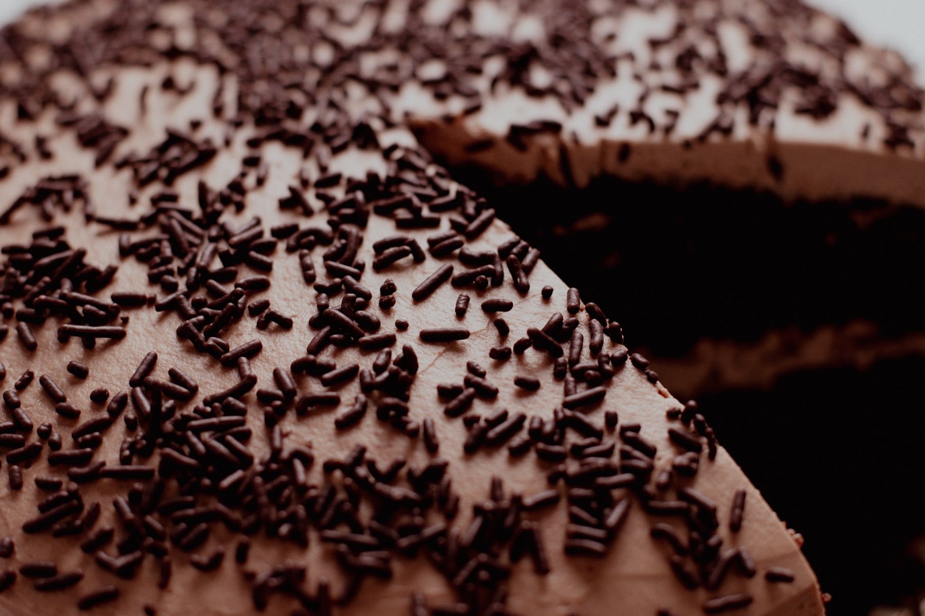 Close-up of chocolate sprinkles on a frosted cake with a slice cut out