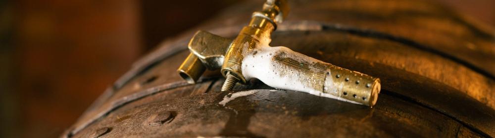 A brass tap set into a wooden cask, froth around its base