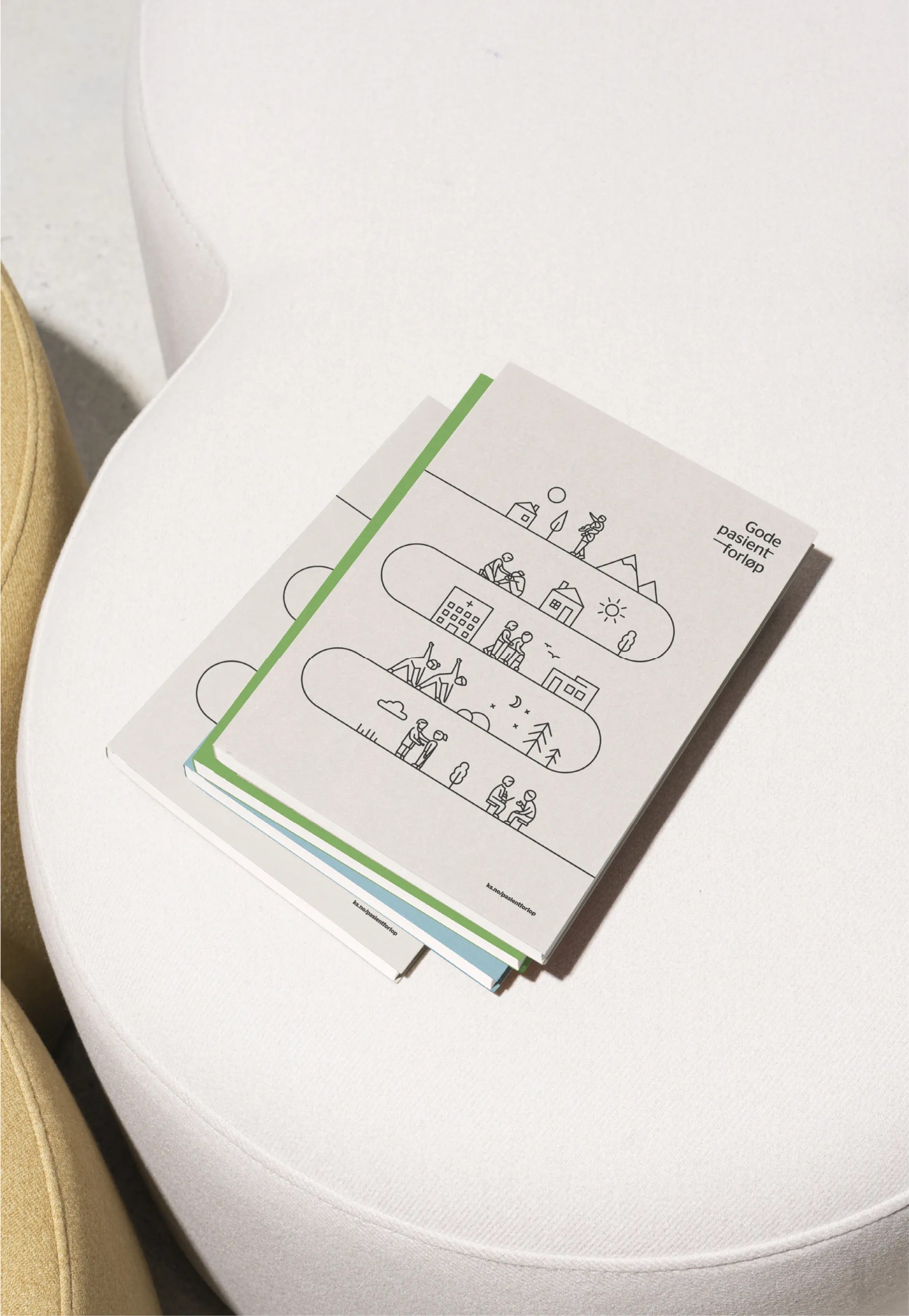 Stack of booklets with minimalist line illustrations and the text 'Gode pasientforløp' on a white chair.