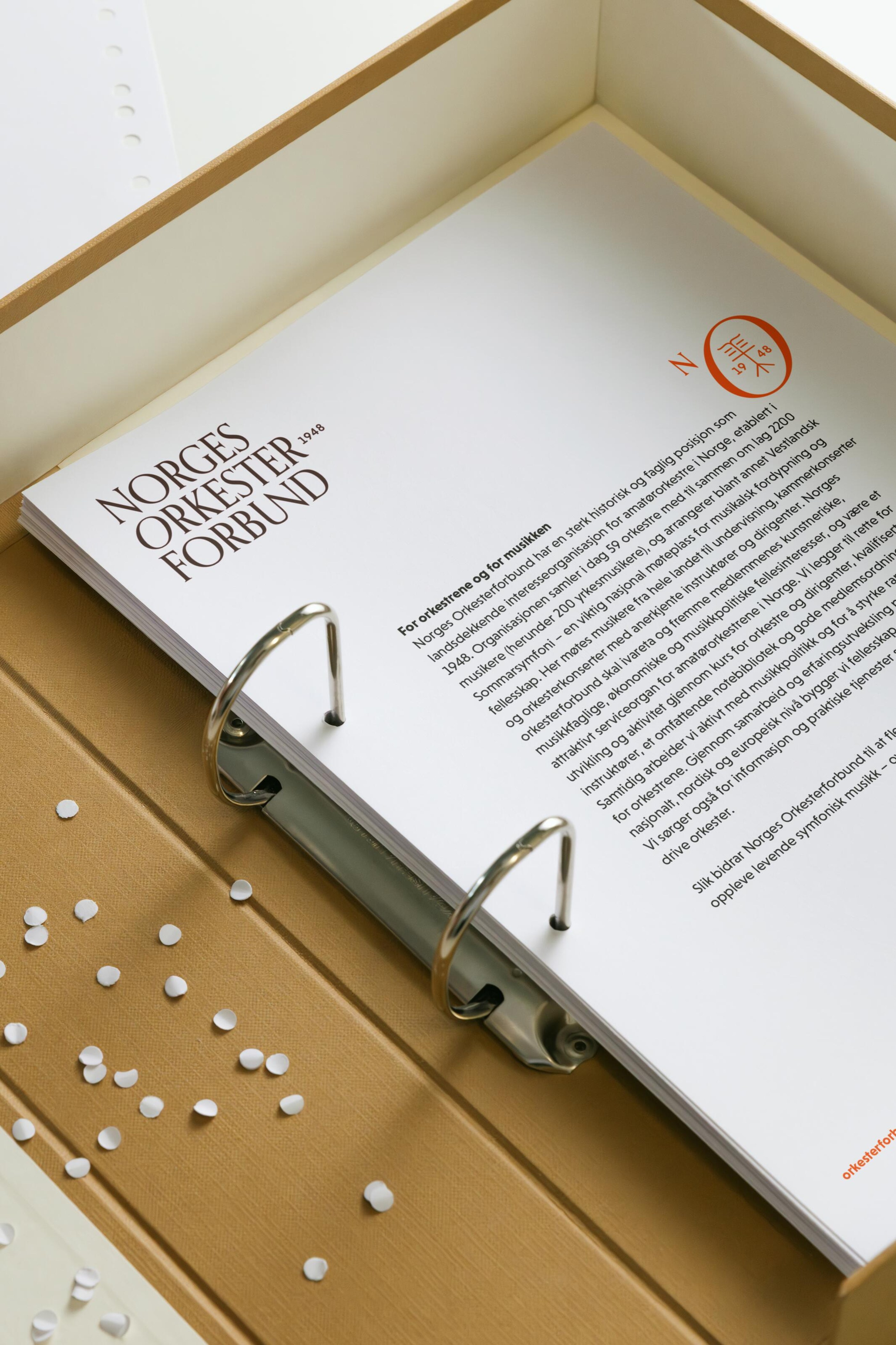Open ring binder showing the Norges Orkesterforbund wordmark, orange secondary symbol and an About us page.