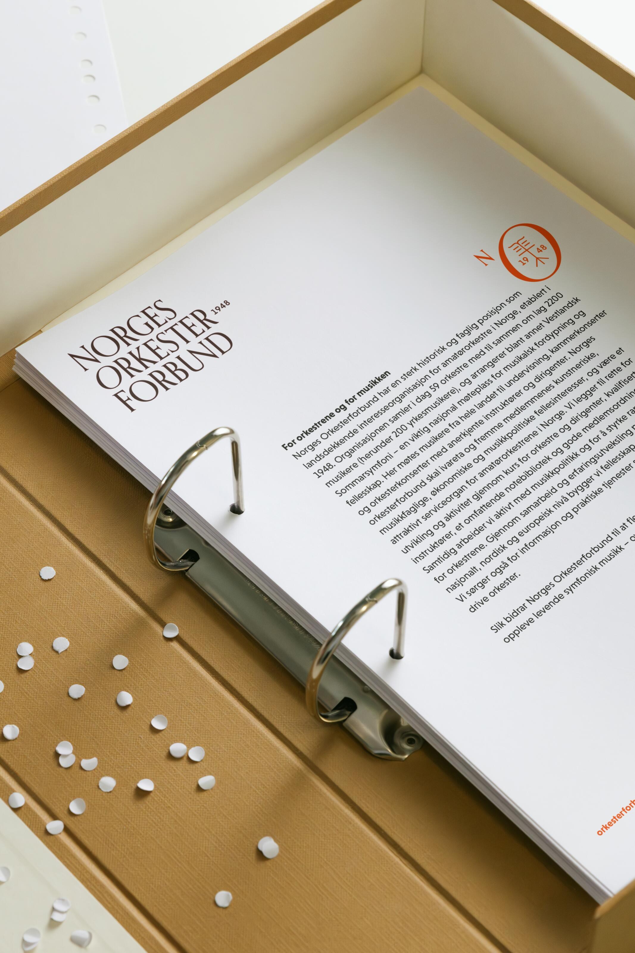 Open ring binder showing the Norges Orkesterforbund wordmark, orange secondary symbol and an About us page.