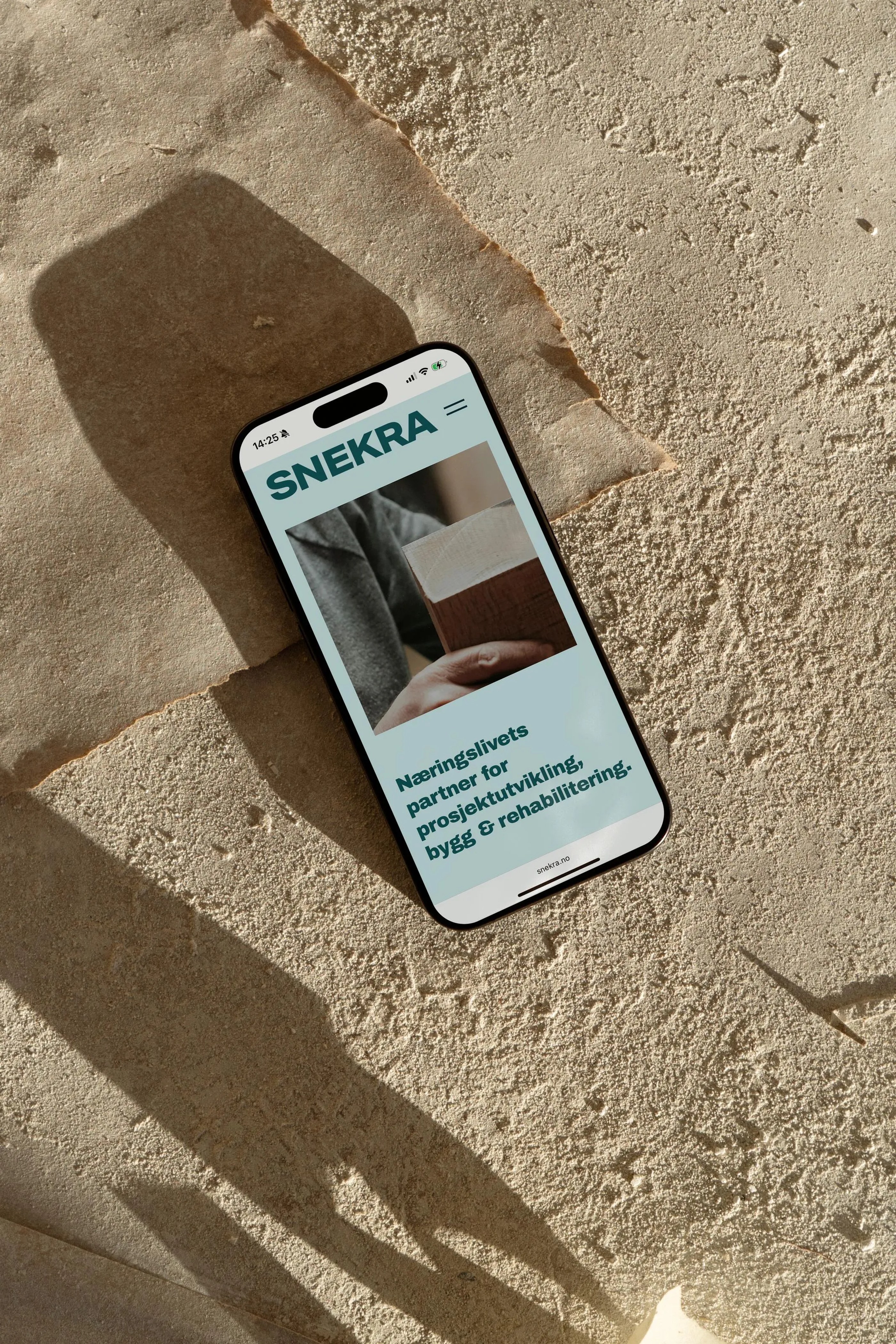 Smartphone on textured stone surface displaying Snekra website with text about project development and construction partnership.