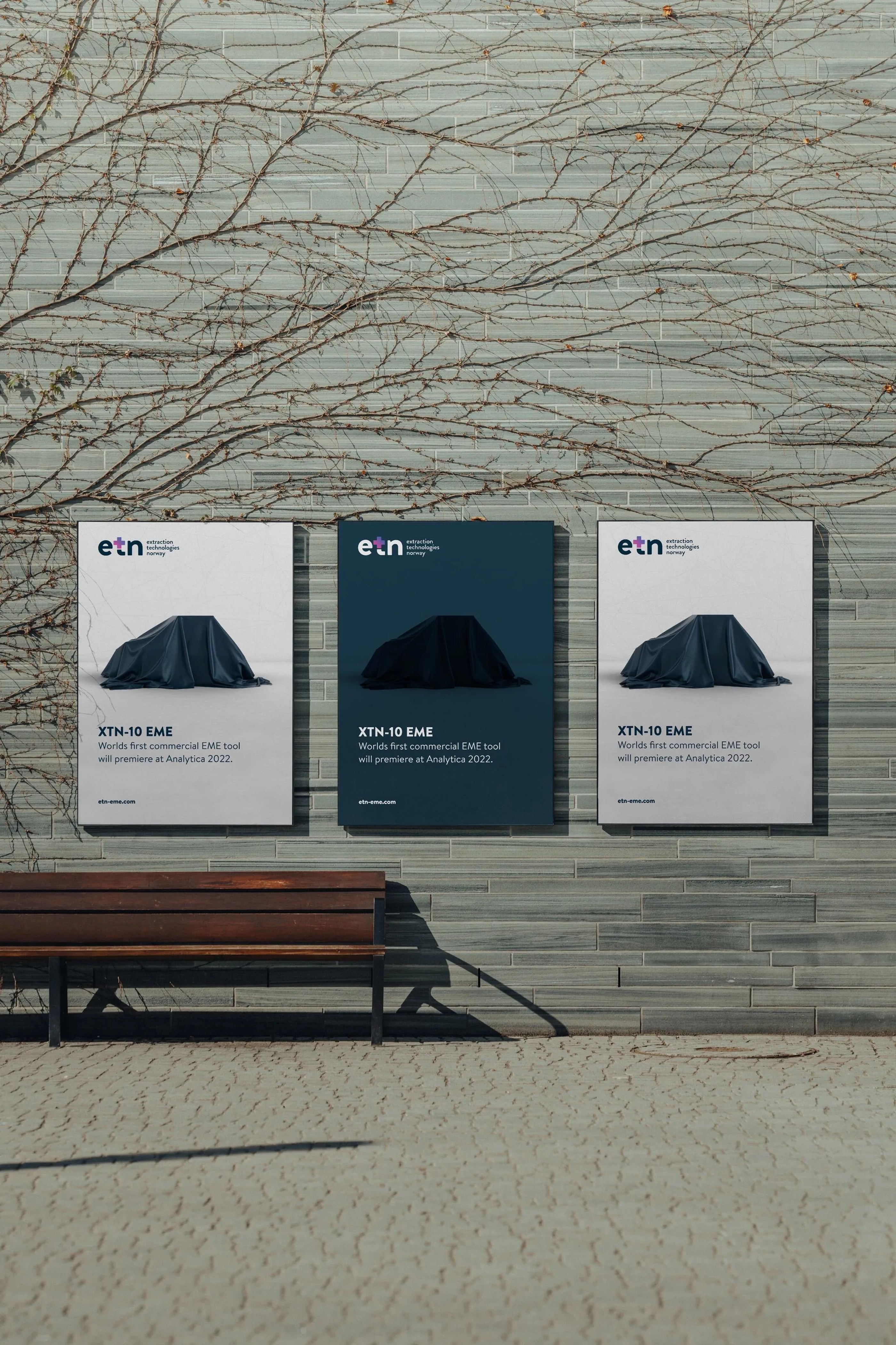 Three promotional posters for ETN's XTN-10 EME tool display on a wall above a wooden bench, featuring a covered object silhouette.