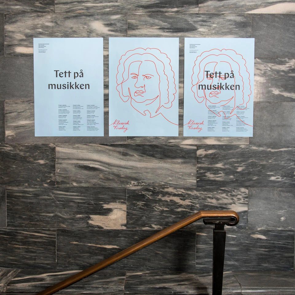 Three light blue posters on a gray marble wall, featuring text in Norwegian and red line drawings of a classical composer's face.