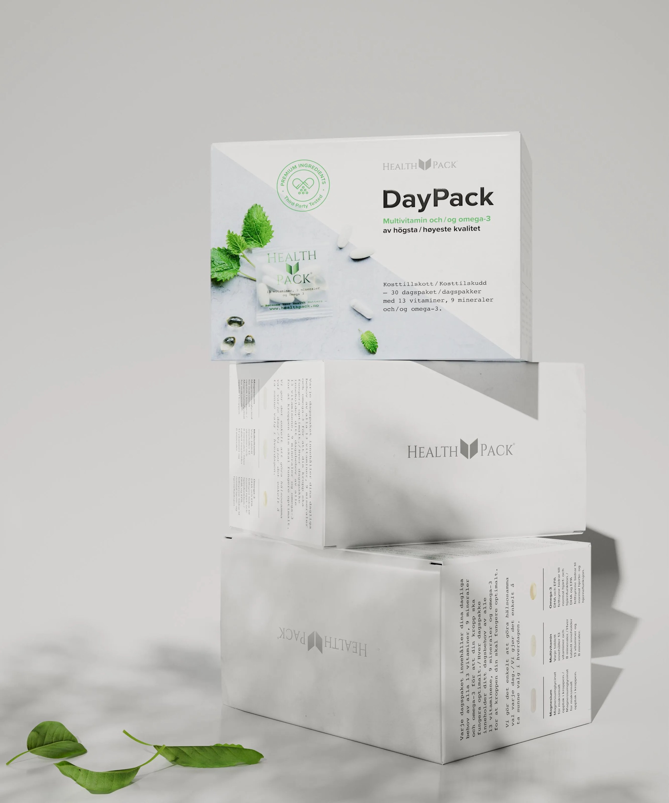 Stack of three white Health Pack DayPack multivitamin boxes with green leaves and capsules on top.