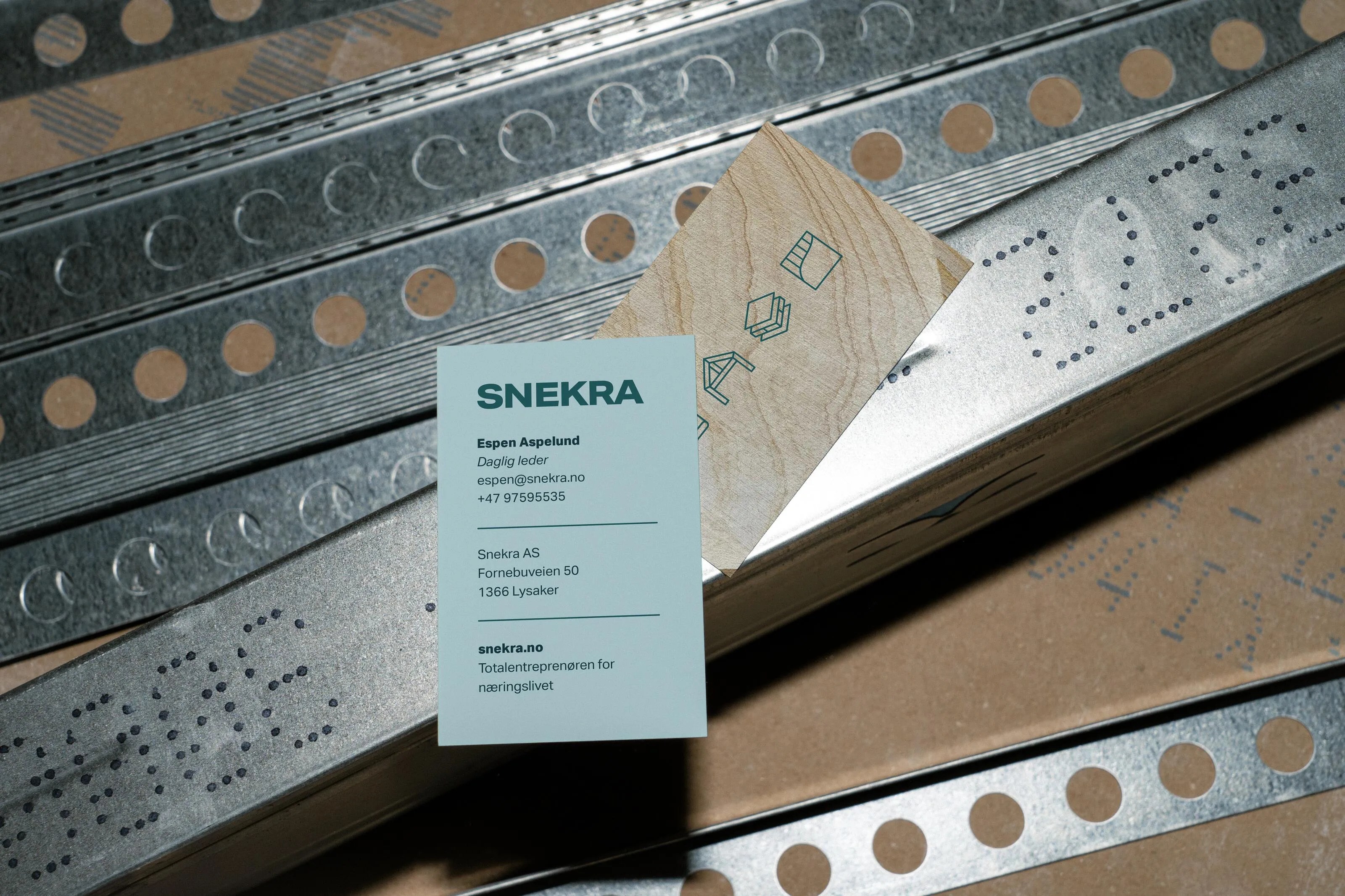 Business card of Espen Aspelund from Snekra, placed on metal construction materials with perforations.