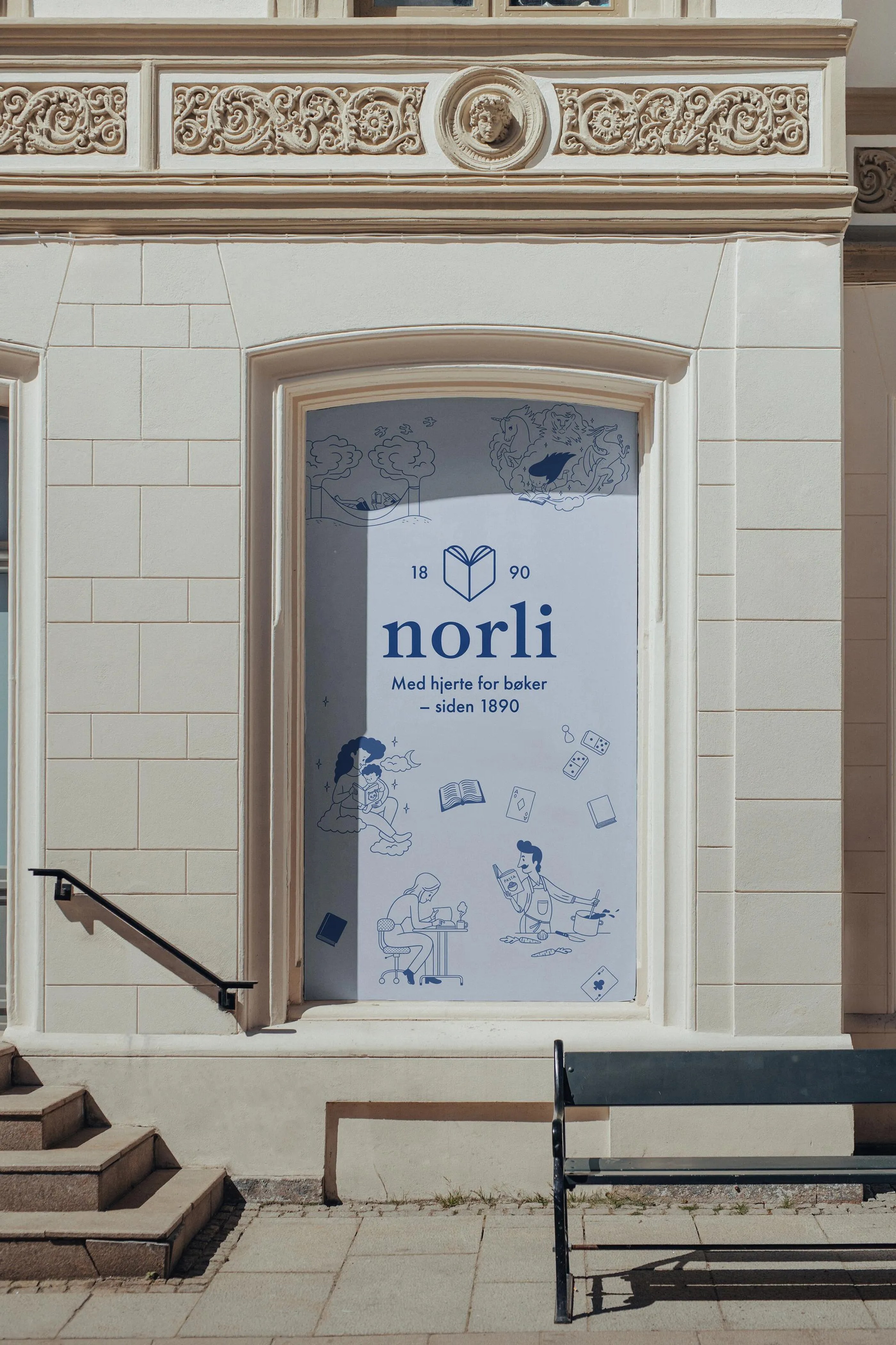 Storefront window covered with a Norli bookstore sign featuring illustrations of people reading and cooking, with text in Norwegian.