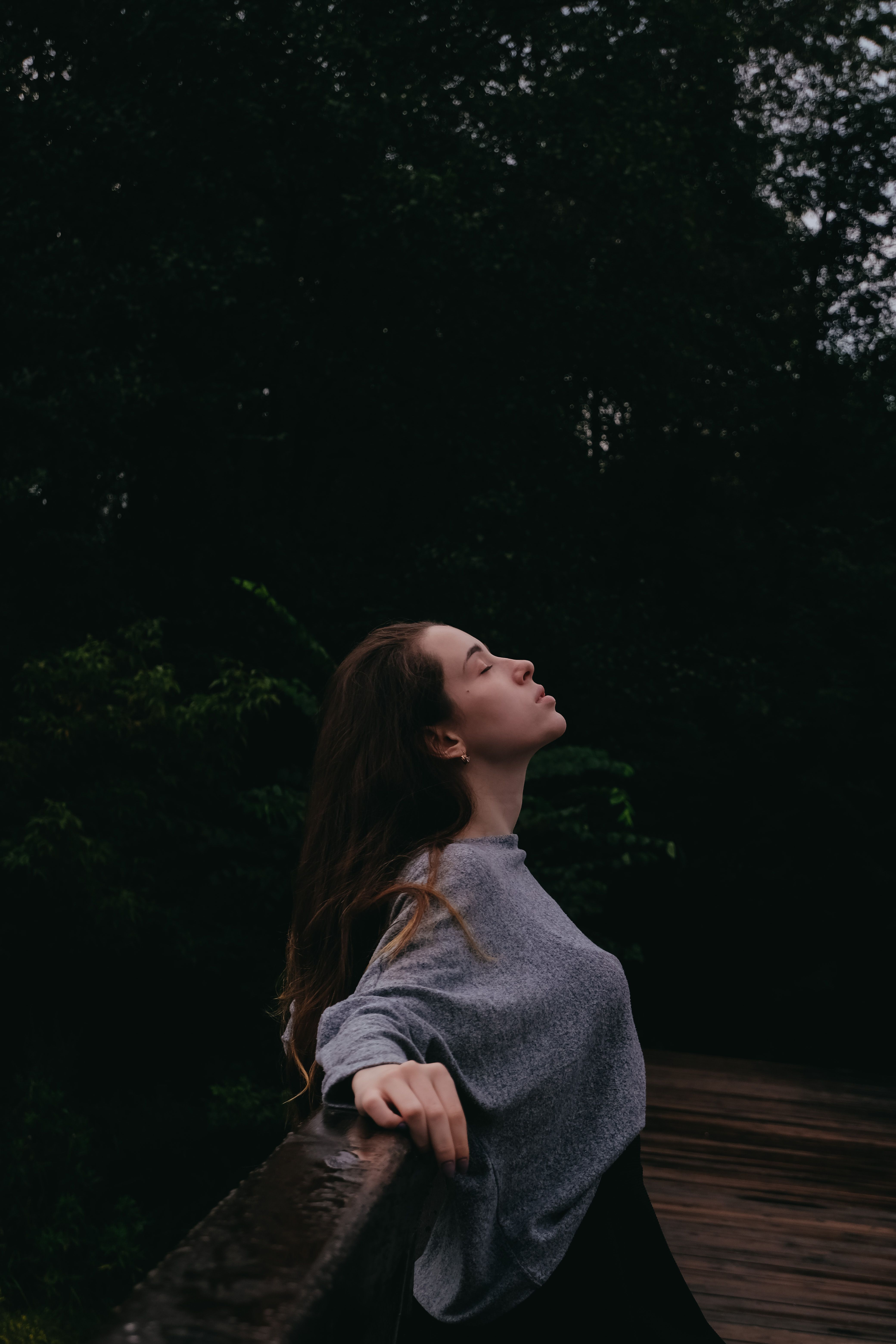 Vrouw met gesloten ogen leunt tegen een houten hek in een groen park