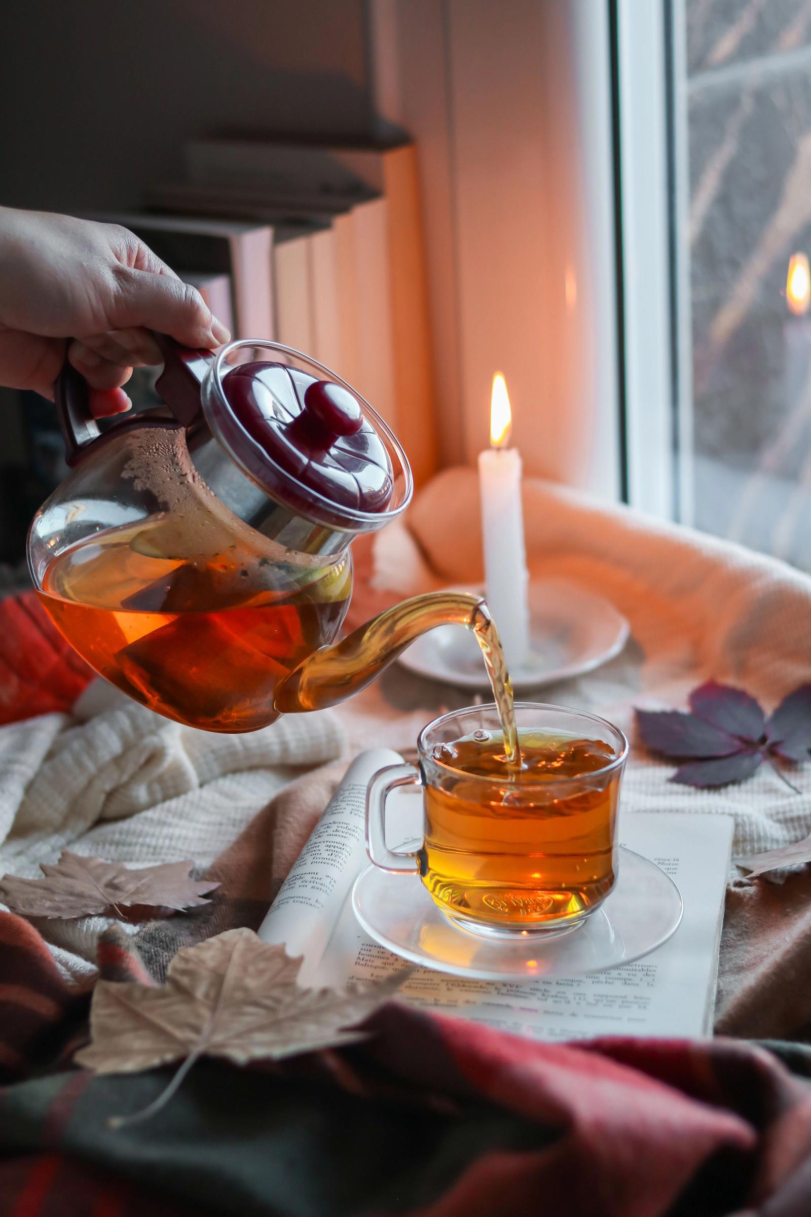 Hand die thee inschenkt bij kaarslicht, met herfstbladeren op tafel