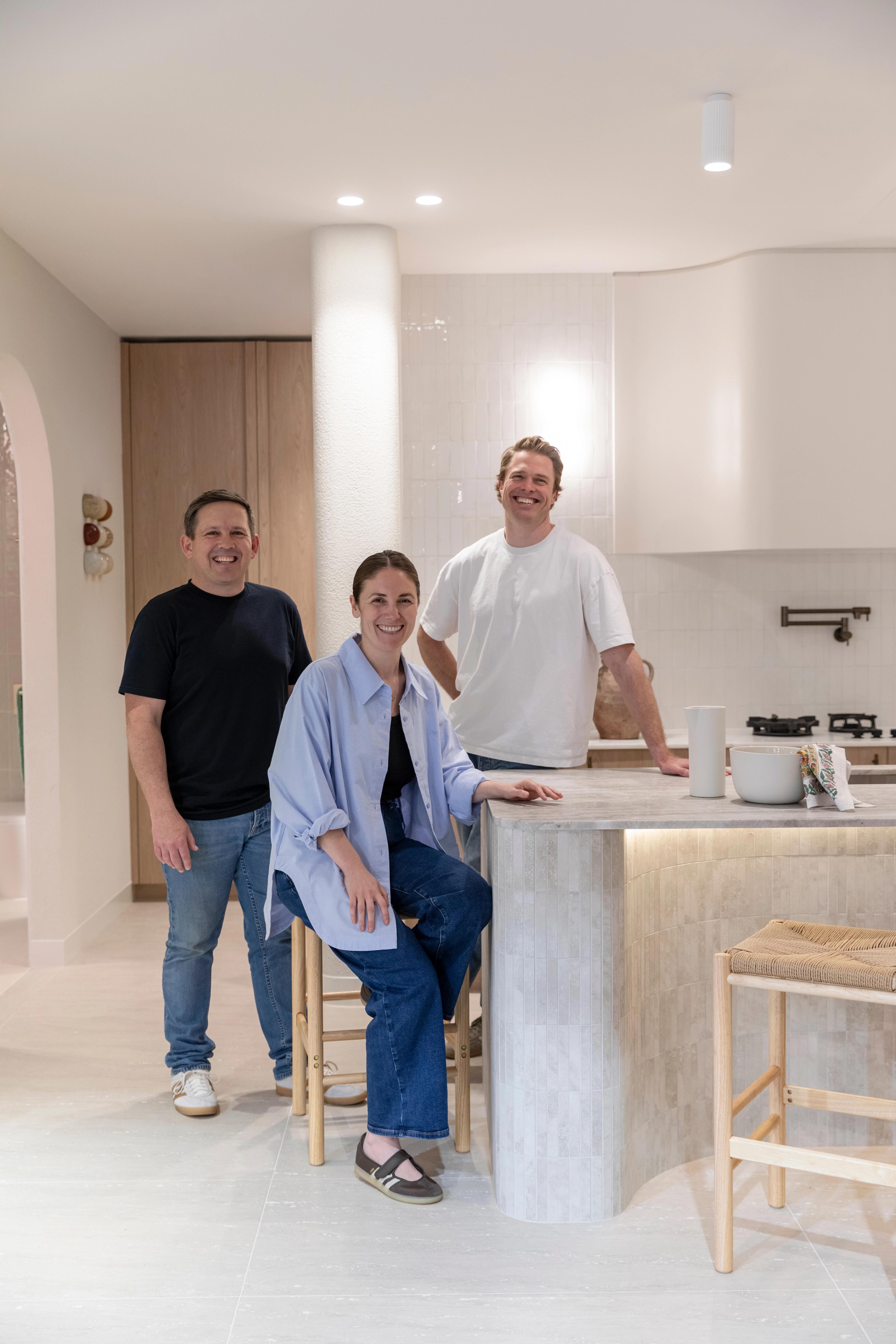 Three people in a bright kitchen with a tiled island, pale cabinetry and pendant lighting
