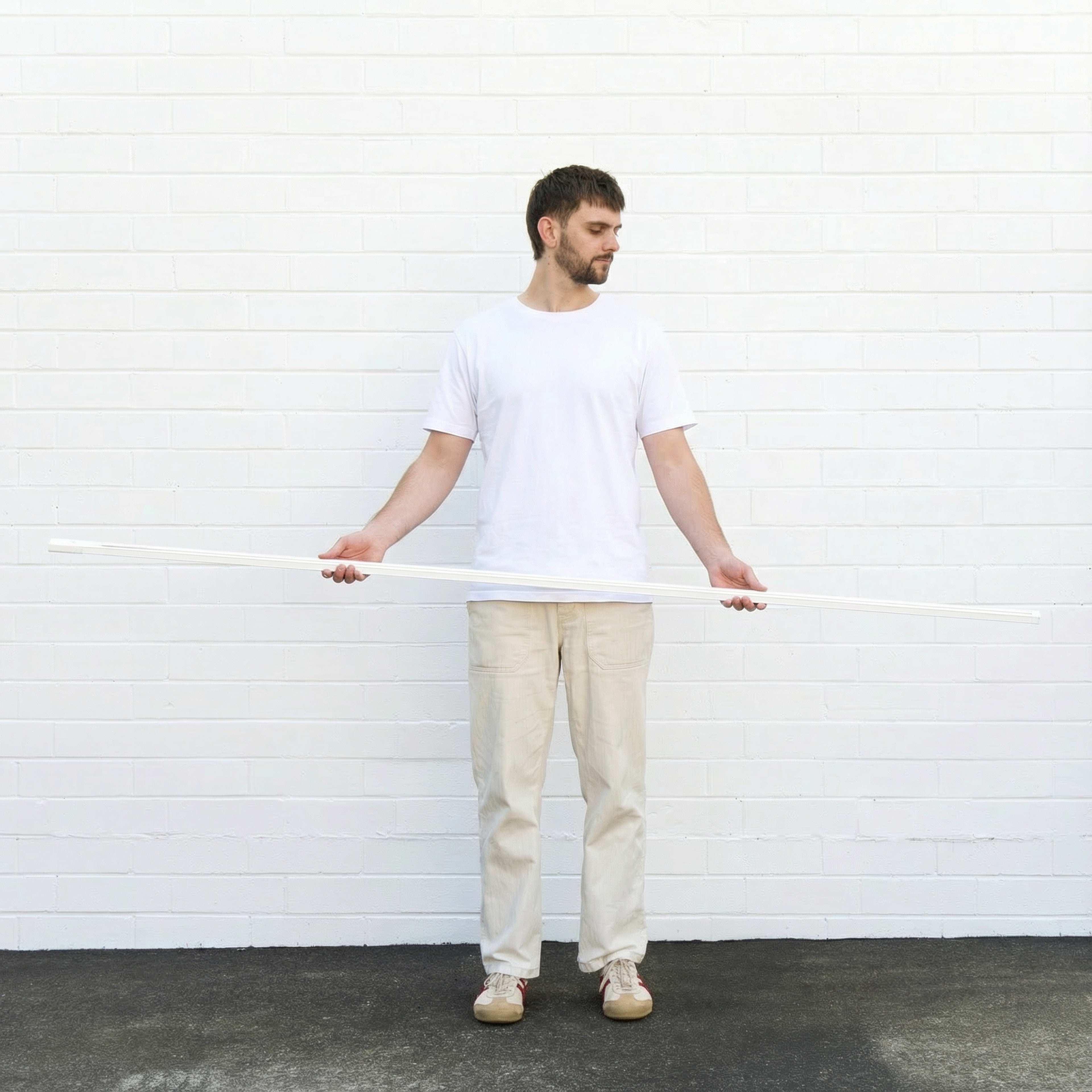 Man holding a long white track light against a white brick wall