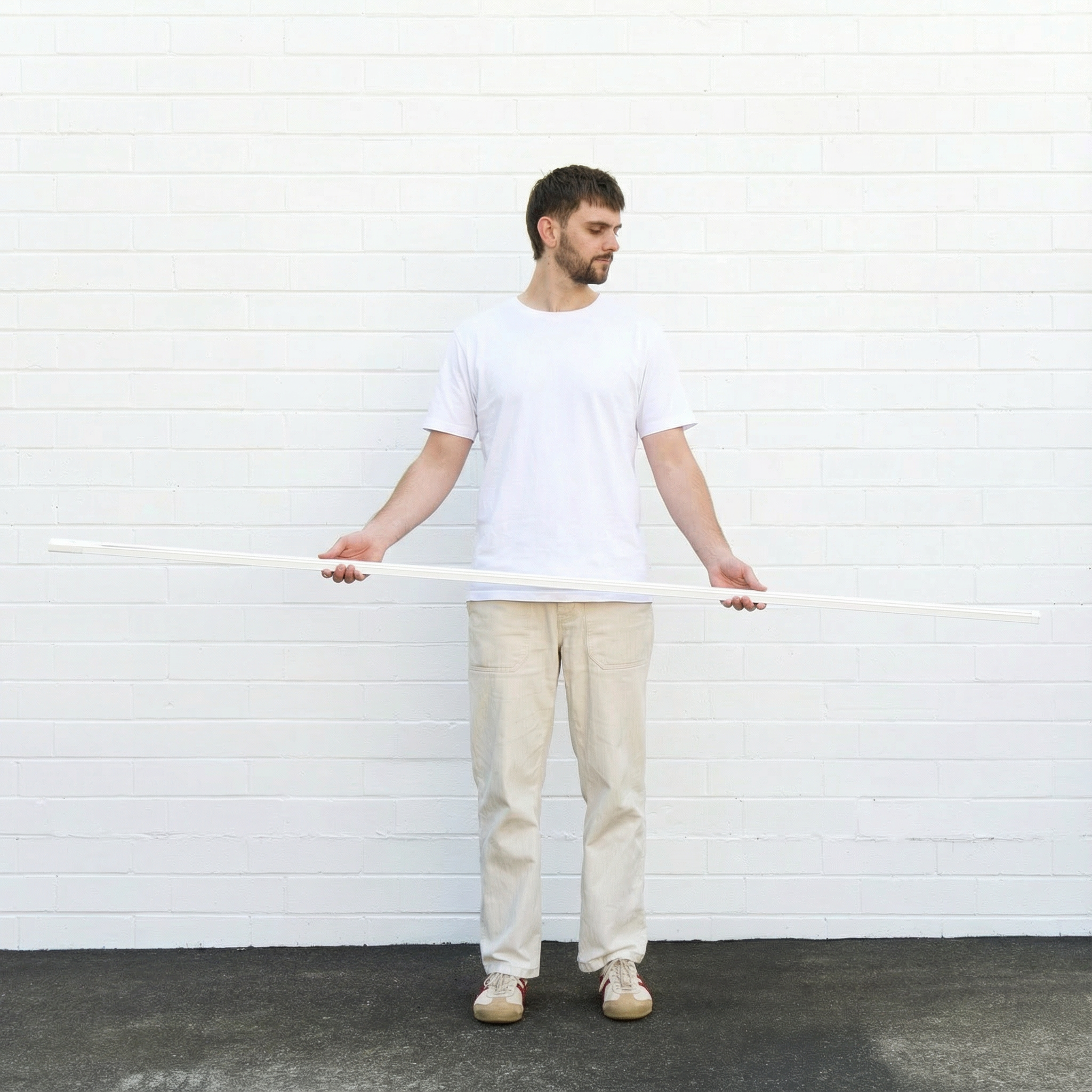 Man holding a long white track light against a white brick wall