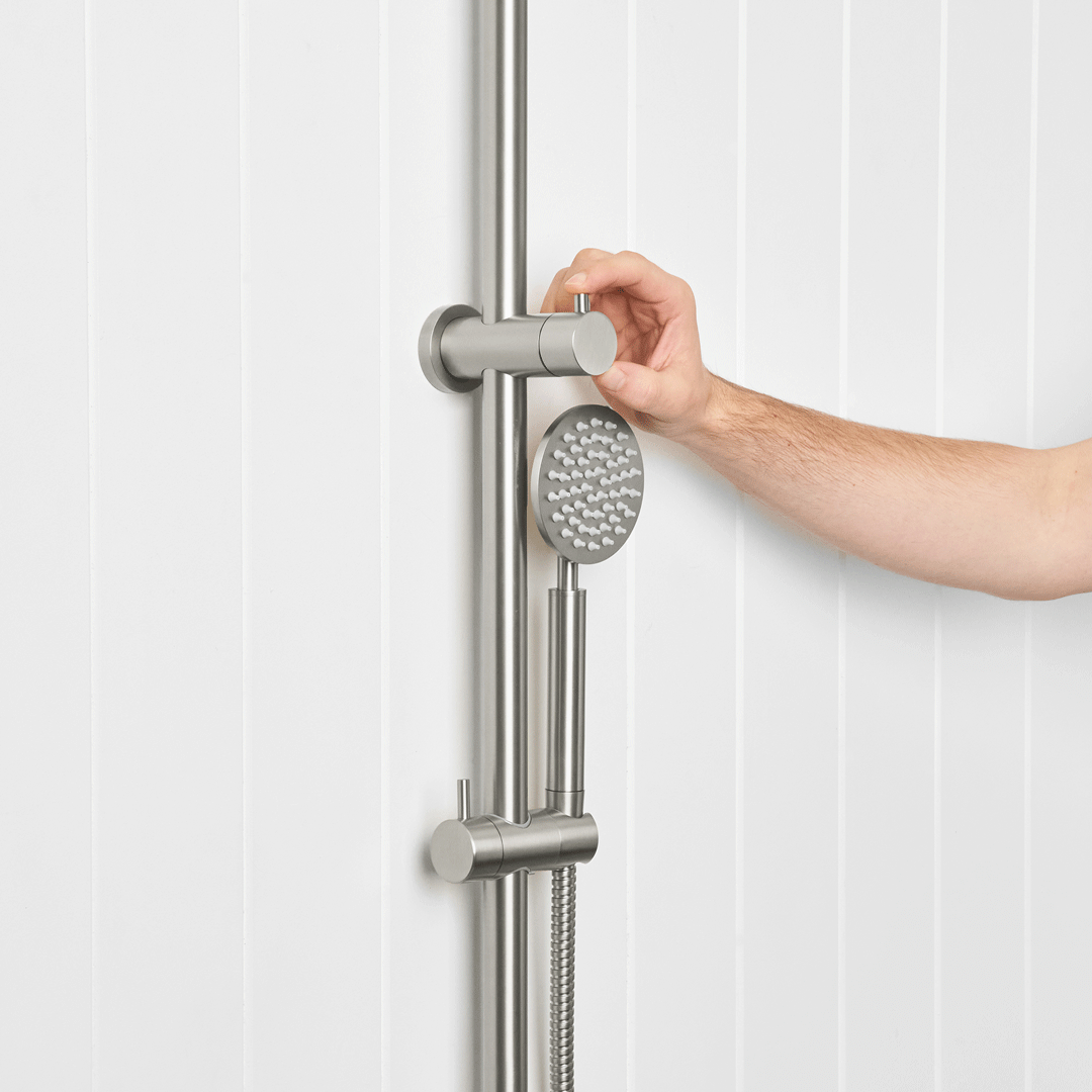 Hand adjusting a brushed metal handheld shower on a rail against white wall panels
