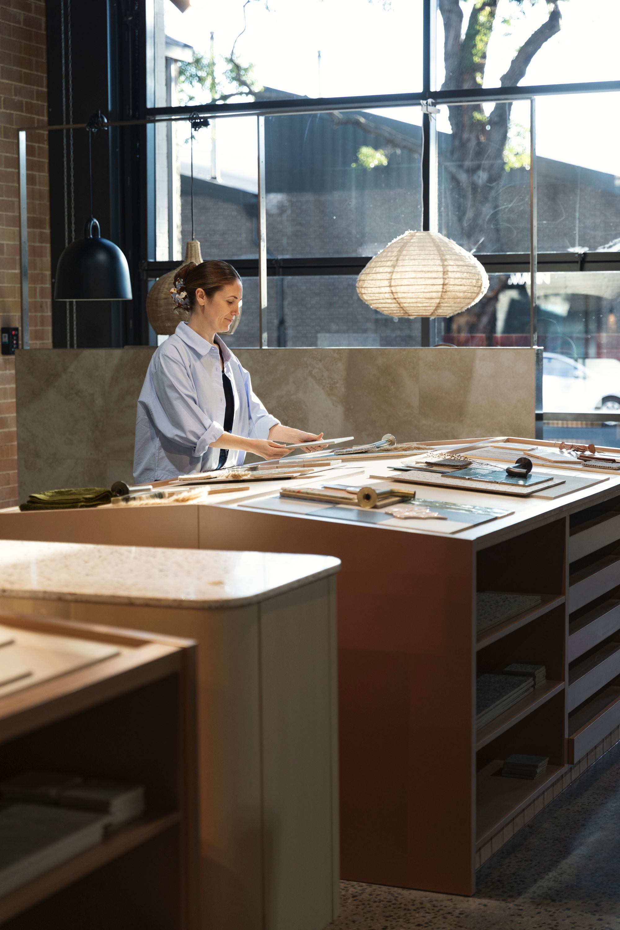 Woman reviewing tile samples at a showroom counter beneath pendant lights
