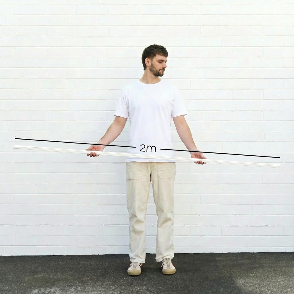 Man holding a long white track light rail against a white brick wall