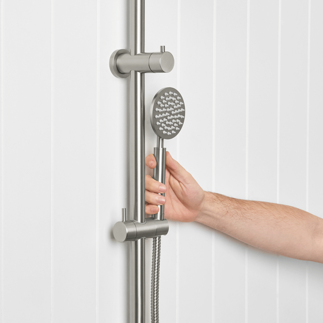 Handheld shower head held beside a vertical rail against white wall tiles