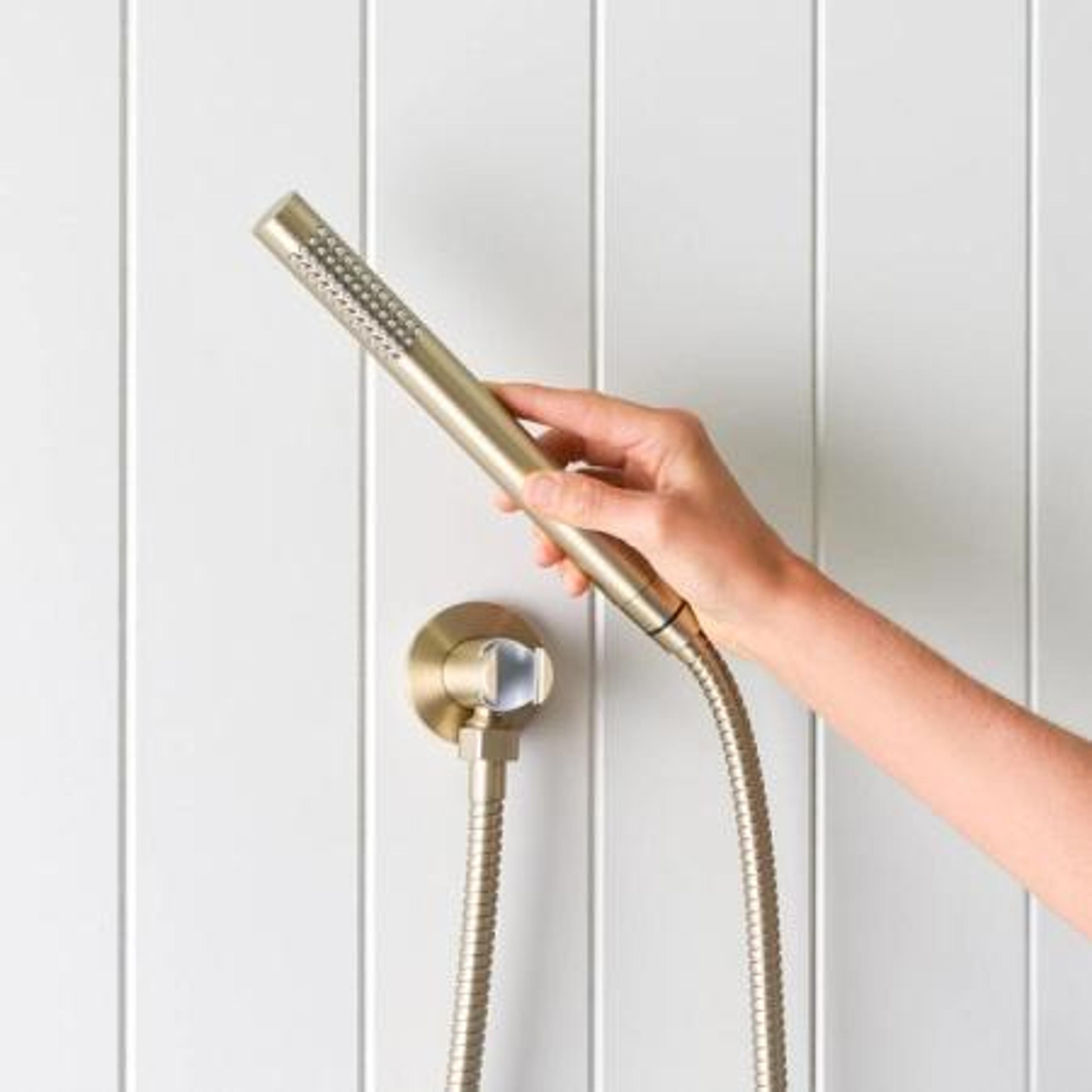Handheld shower head and hose in a brushed brass finish against white wall panels