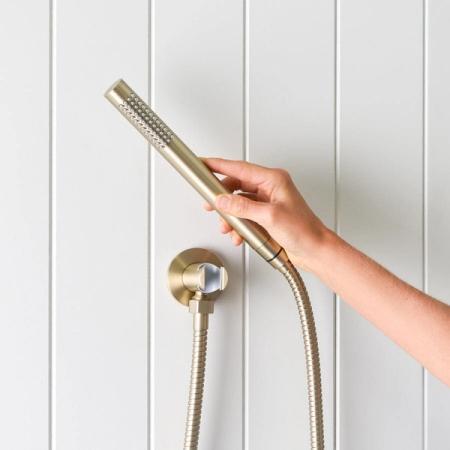Handheld shower head and hose in a brushed brass finish against white wall panels