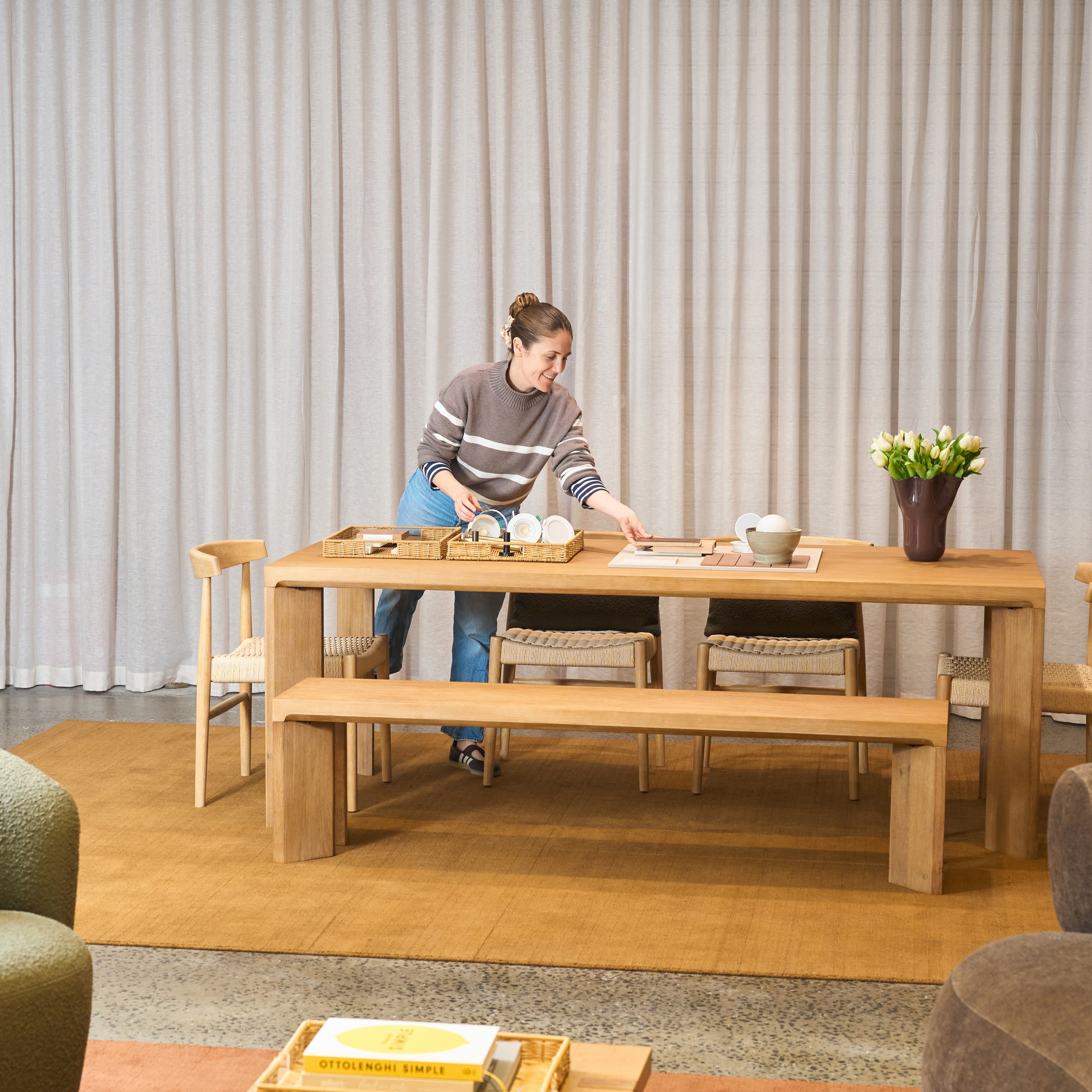 Woman arranging tableware on a timber dining table in a furnished showroom