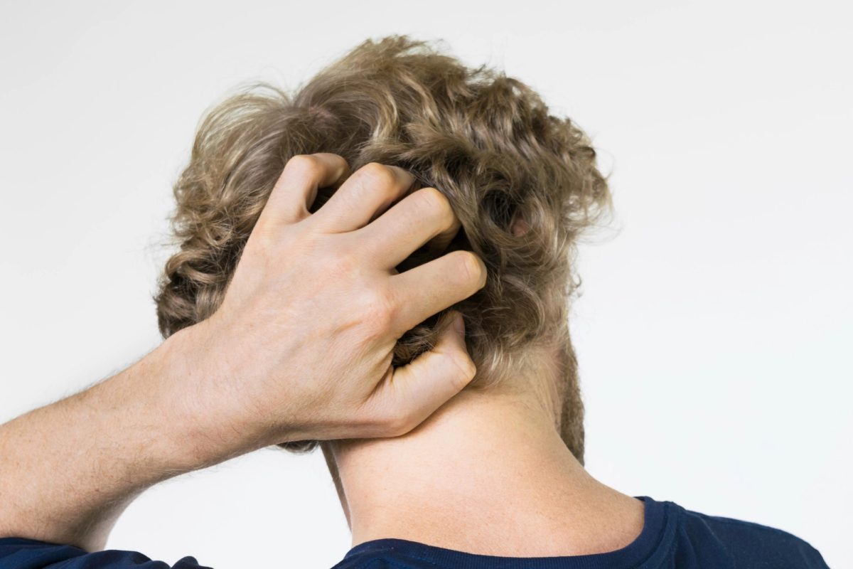 Personne vue de dos portant une main à son cuir chevelu, sans visage visible.