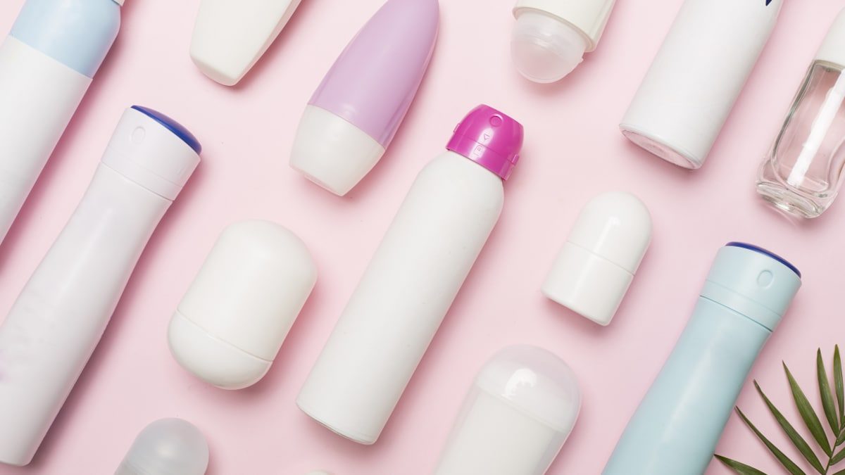 Déodorants en stick, roll-on et spray disposés sur un fond rose.