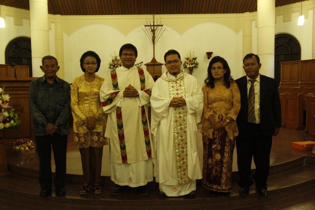 Dua imam berbusana liturgi berfoto bersama dua pria dan dua wanita berkebaya di depan altar gereja.
