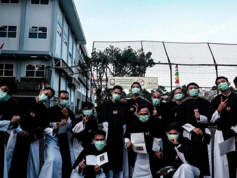Para frater Krosier bermasker berpose bersama sambil memegang buku kecil di halaman sebuah sekolah.