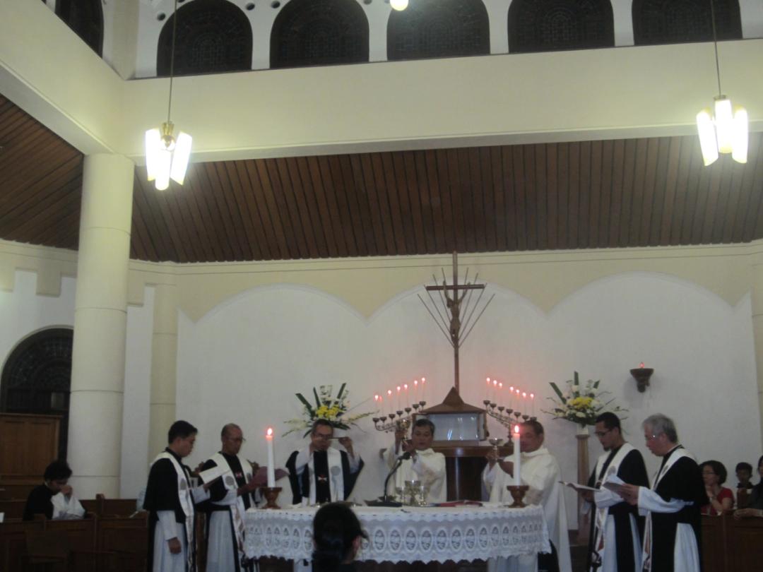 Para Krosier berstola merayakan Ekaristi mengelilingi altar bundar di kapel, dengan salib dan lilin di belakang.
